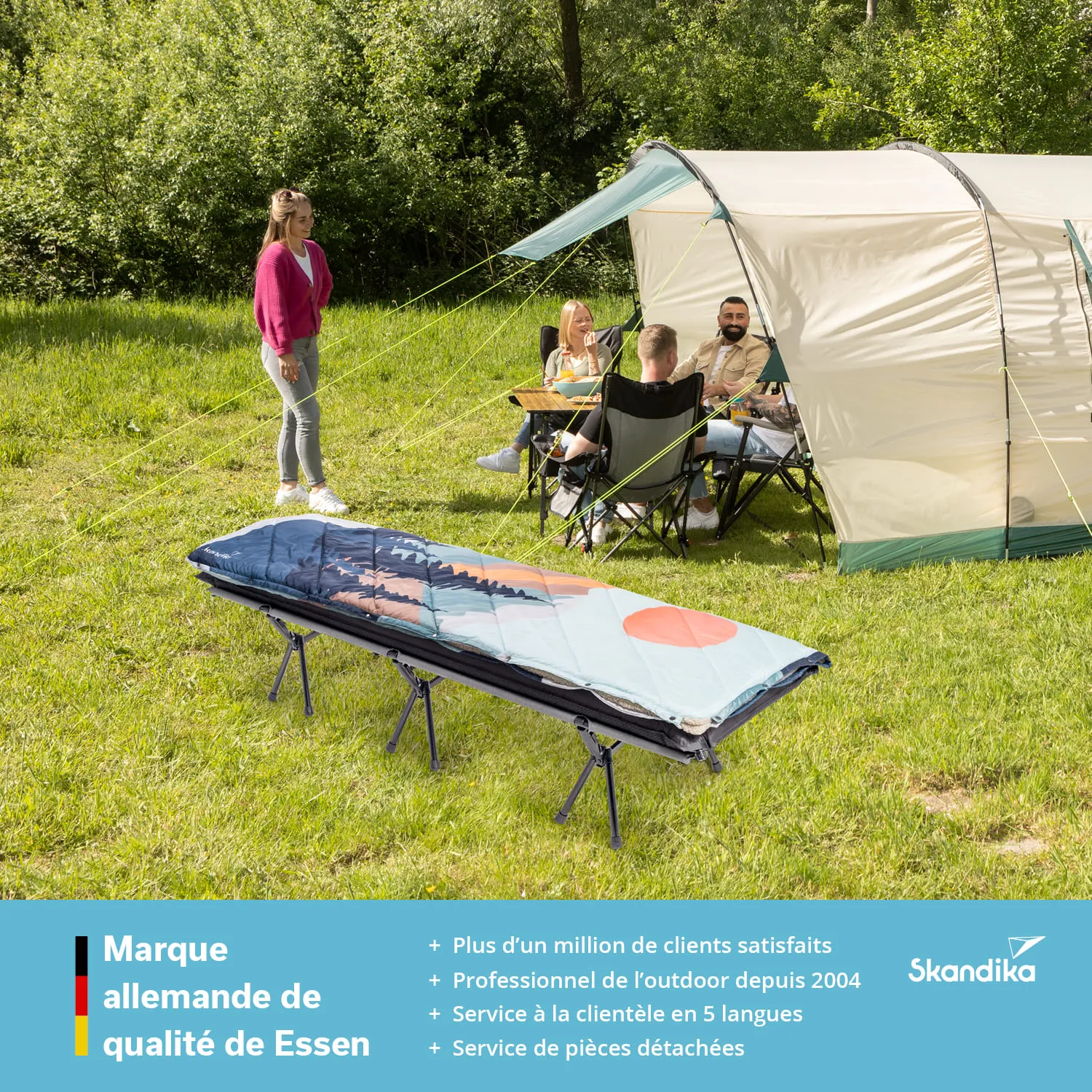 Zelt auf einer Wiese, vier Personen sitzen im Schatten, eine Person steht nahe einem ausgeklappten Feldbett.
