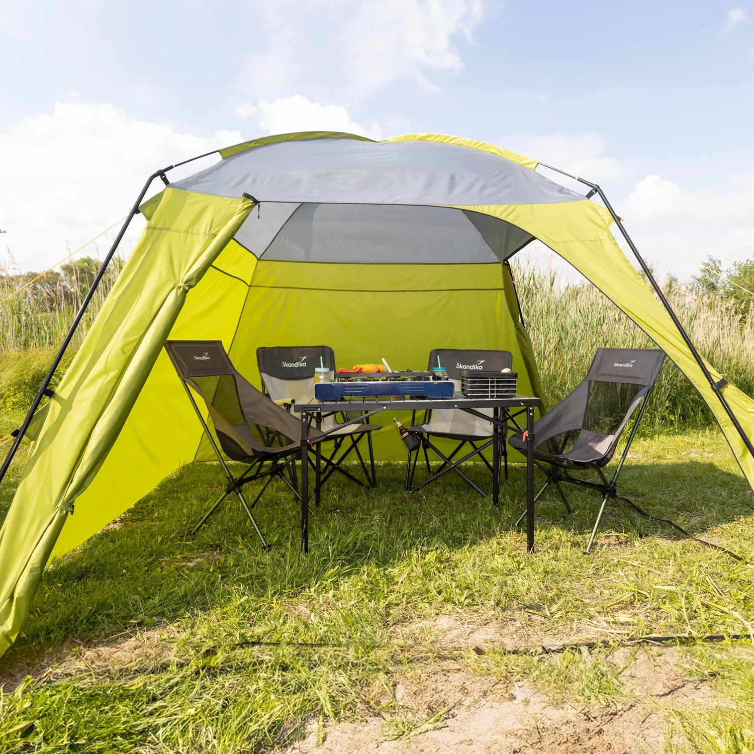 Grüne Gartenlaube mit Tisch und zwei Klappstühlen. Auf dem Tisch steht ein Gaskocher. Im Hintergrund hohe Gräser.