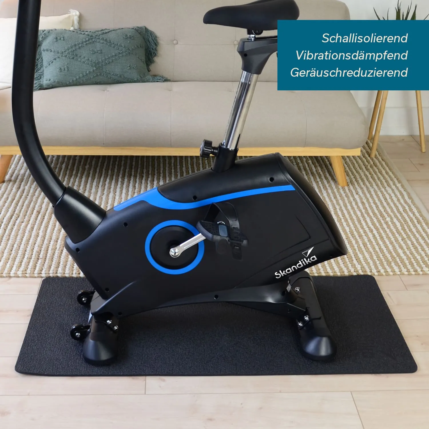 Ein Ergometer mit schwarzem Gehäuse und blauen Akzenten steht auf einem dunklen Unterlage. Im Hintergrund ist ein helles Sofa zu sehen.