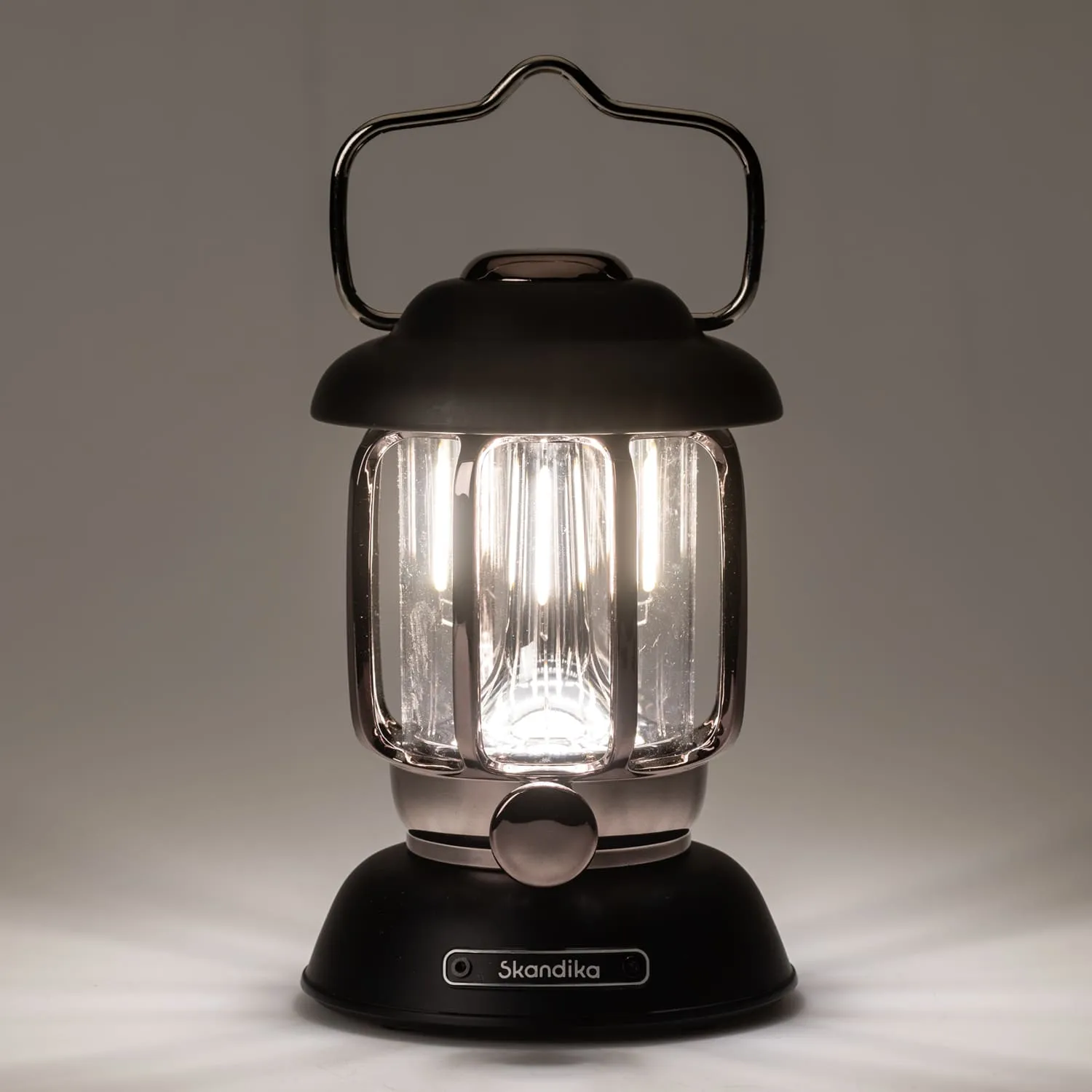 Tischlampe mit transparentem Gehäuse, schwarzem Sockel und Tragegriff. Leuchtmittel erhellt die Umgebung.