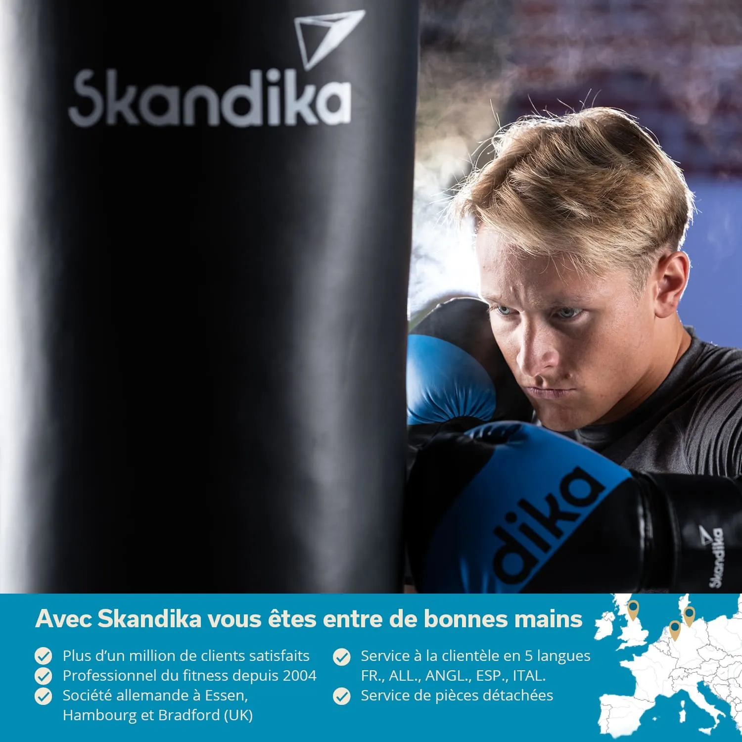Person mit blonden Haaren trägt blaue Boxhandschuhe und konzentriert sich auf einen schwarzen Boxsack mit dem Schriftzug „Skandika“.