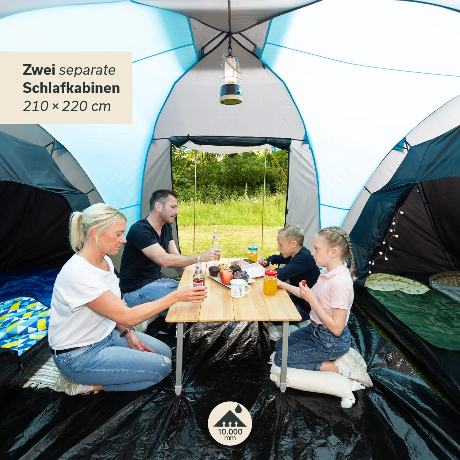 Familie sitzt in einem Zelt an einem Tisch mit Getränken und Snacks. Zwei Schlafkabinen sind sichtbar.