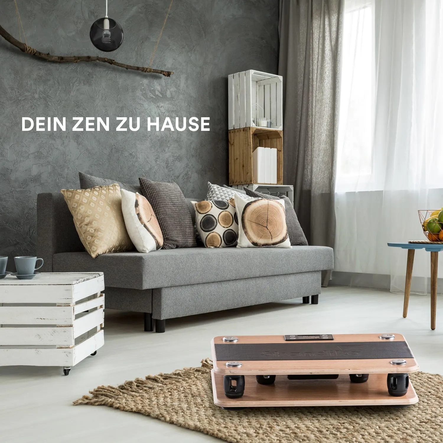 Graues Wohnzimmer mit einer Couch, Kissen und einem kleinen Tisch. Ein Teppich und Holzregale sind sichtbar.