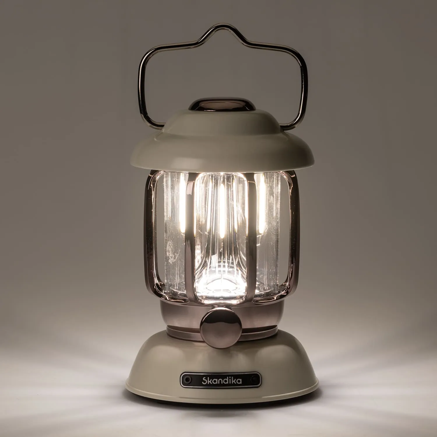 Öl-Lampe in beige und Kupfer mit transparentem Glas und einem Griff. Beleuchtet vor einem grauen Hintergrund.