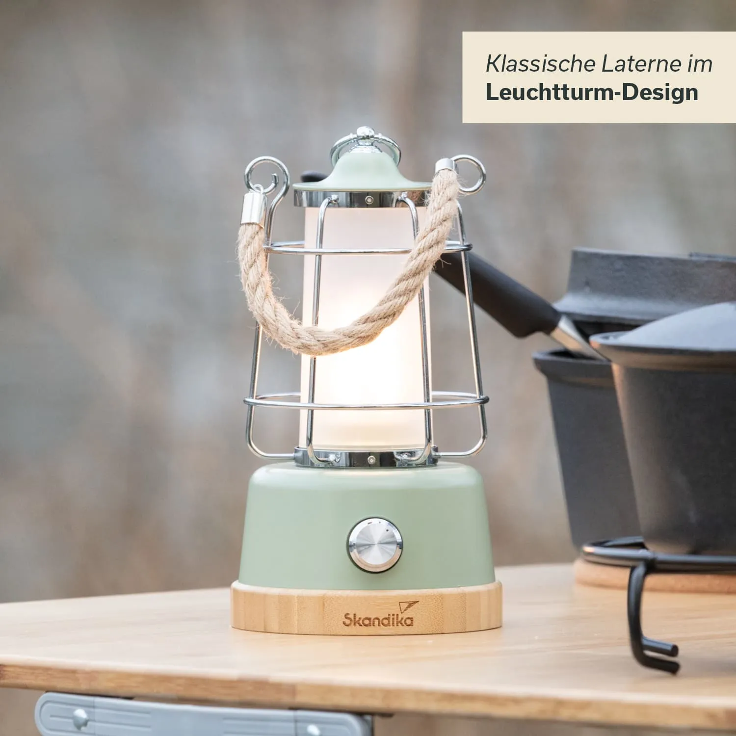 Klassische Laterne im Leuchtturm-Design mit Metallgitter und Seilgriff, steht auf einem Holztisch neben Kochutensilien.