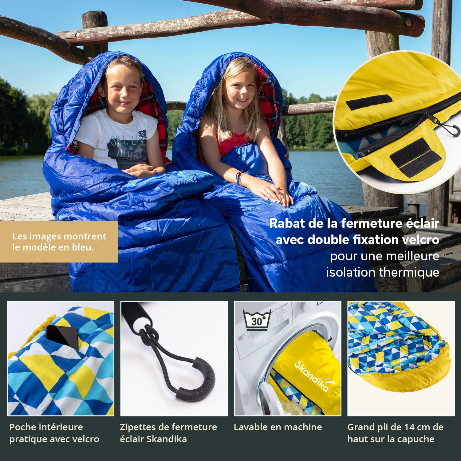Zwei Kinder sitzen auf einem Holzsteg am Wasser, eingewickelt in blaue Schlafsäcke. Hintergrund zeigt Bäume und einen klaren Himmel.