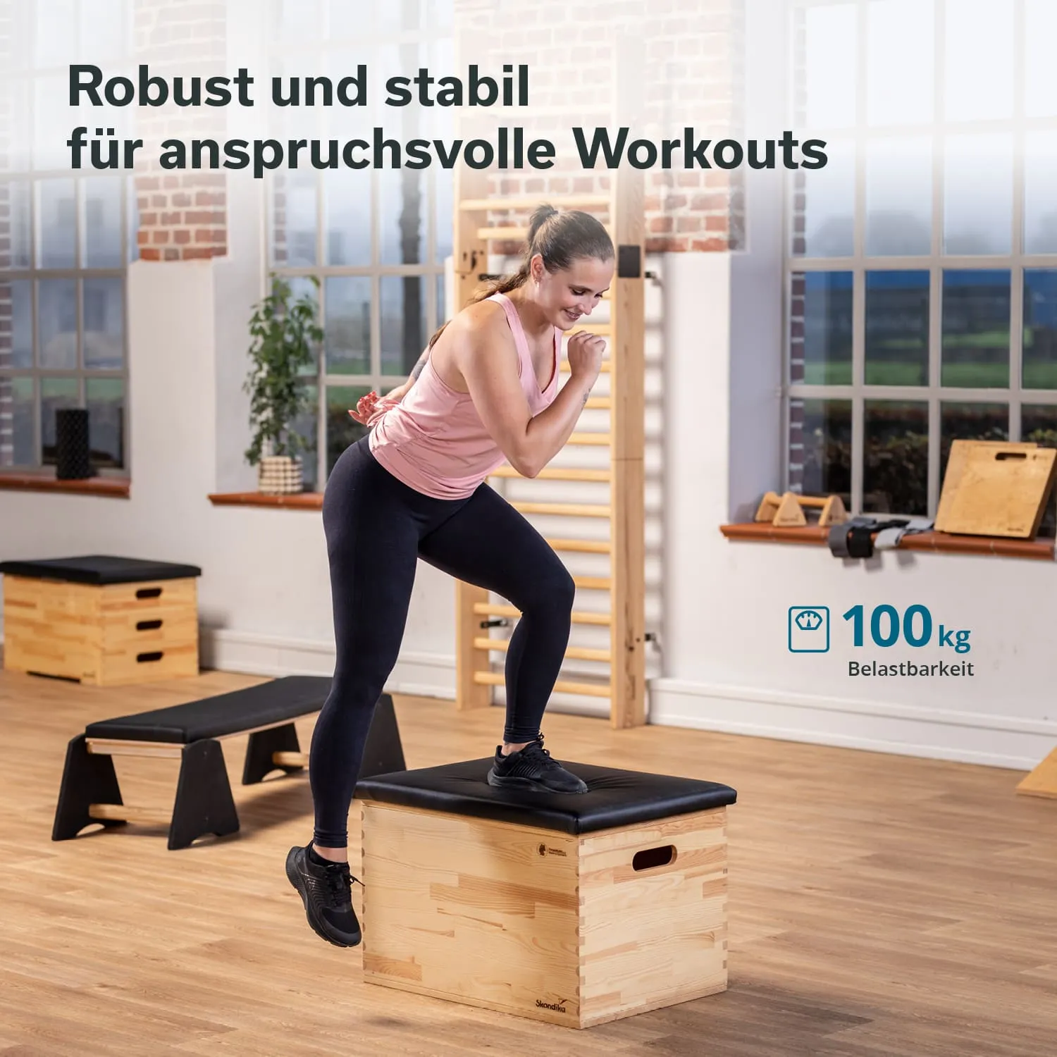 Person steht auf einer stabilen Holzbox und bereitet sich auf einen Sprung vor. Im Hintergrund sind weitere Fitnessgeräte sichtbar.