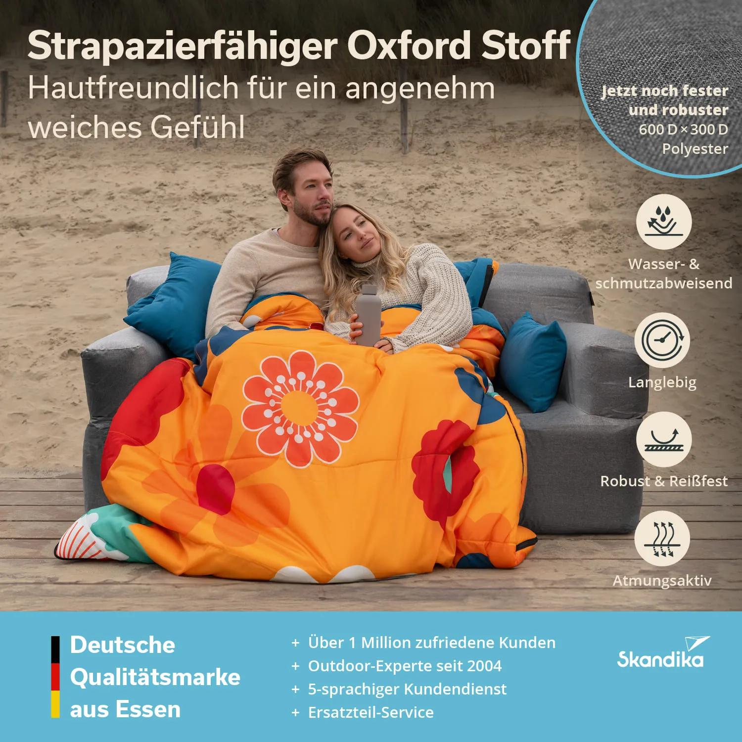 Eine Person und eine Person sitzen auf einer Couch im Freien, eingekuschelt in eine bunte Decke mit floralen Mustern.