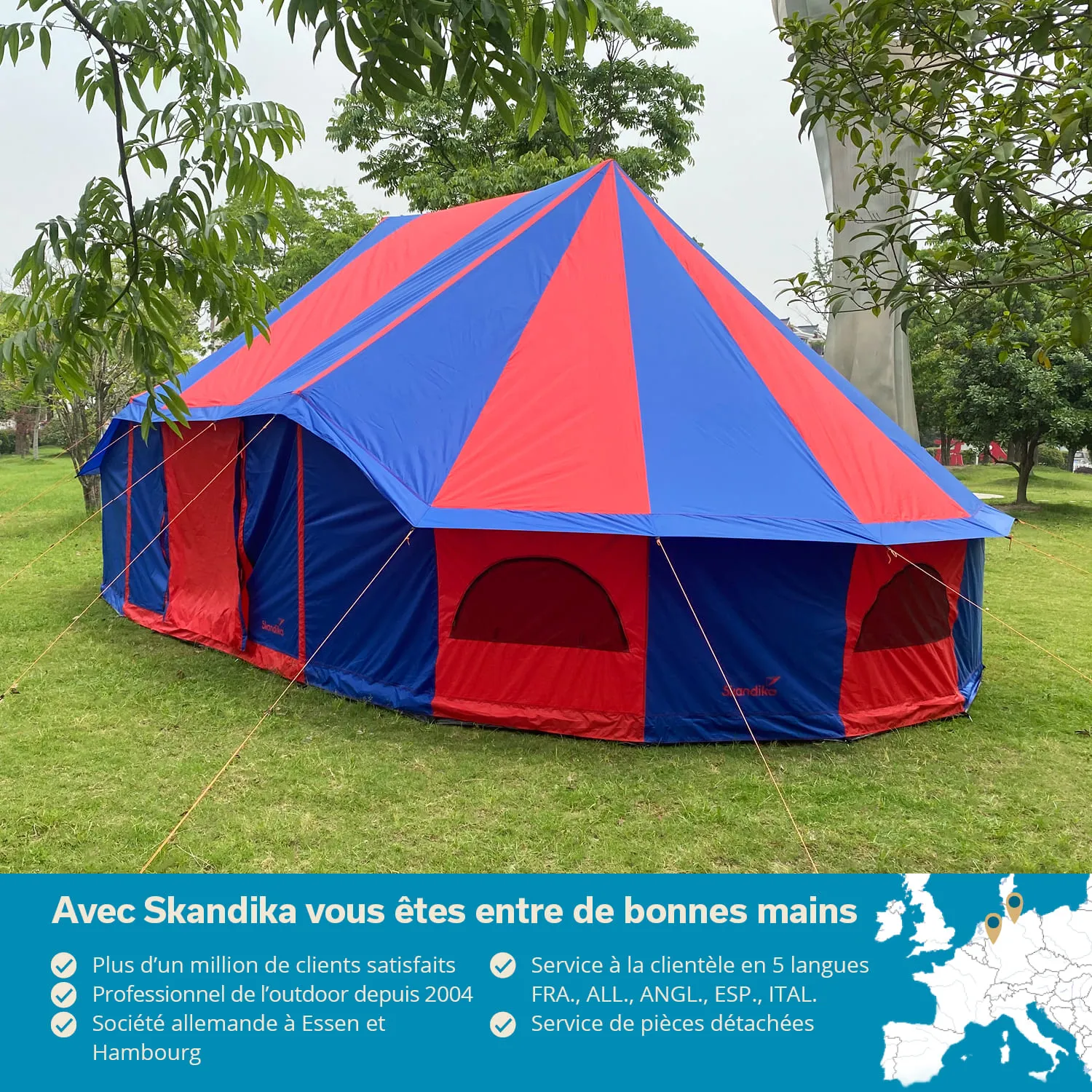 Buntes Zelt mit einem blau-rot gestreiften Dach, umgeben von Bäumen auf einer Wiese.
