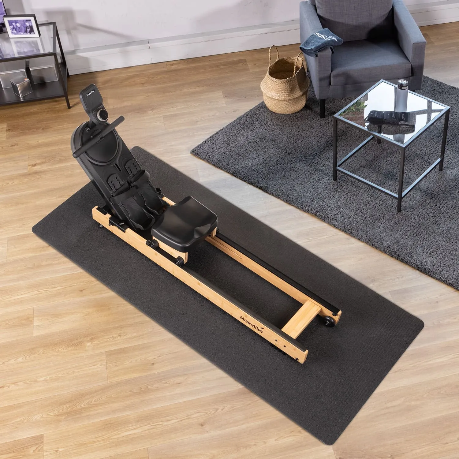 Rudergerät aus Holz mit schwarzer Sitzfläche auf einer Matte. Im Hintergrund ein Sessel und ein Couchtisch auf einem Teppich.