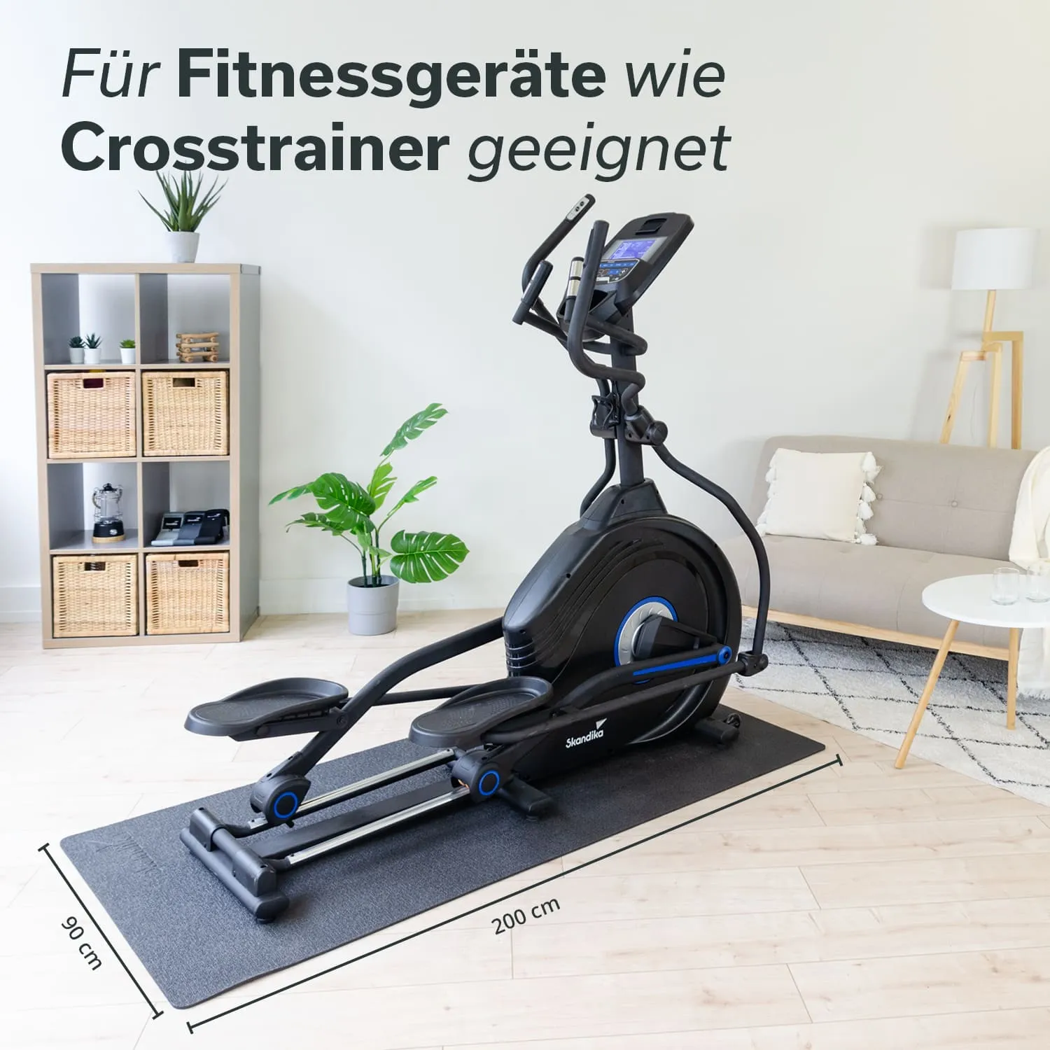 Crosstrainer auf einer Matte in einem hellen Raum mit Pflanzen und einem Sofa in der Ecke. Regale im Hintergrund.