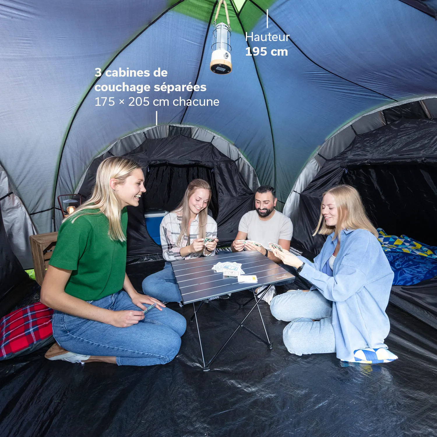 Zeltinnenraum mit vier Personen, die um einen kleinen Tisch sitzen und Karten halten. Die Zeltwände sind schwarz und blau.