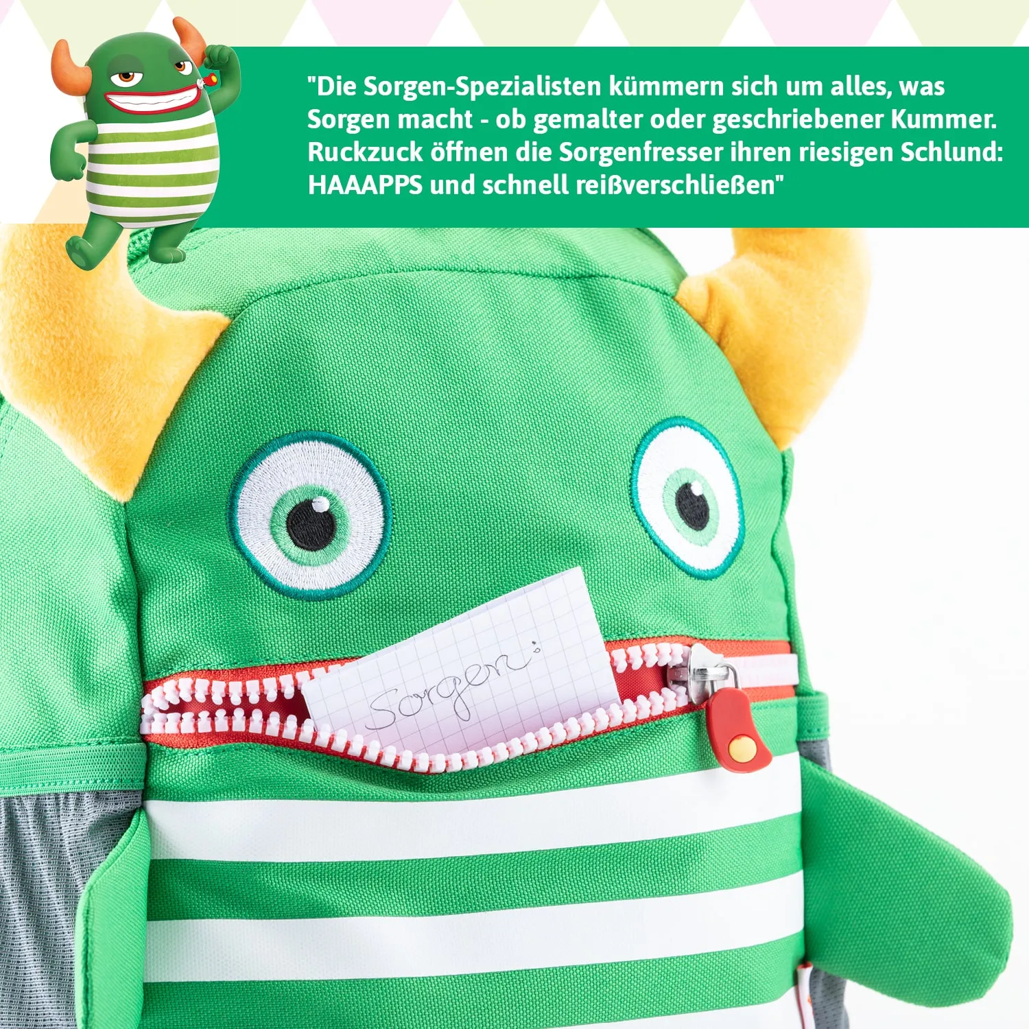 Grüner Rucksack in Form eines Monsters mit großen Augen und Hörnern. Eine Notiz mit dem Wort „Sorgen“ steckt in einem Reißverschlussfach.