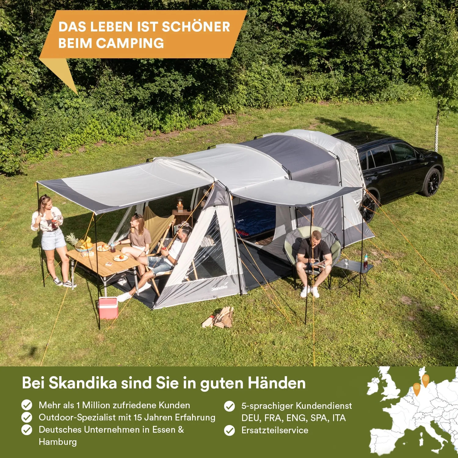 Zelt mit mehreren Ständen auf einer Wiese, Personen sitzen an einem Tisch mit Essen und Getränken, im Hintergrund ein Auto und Bäume.