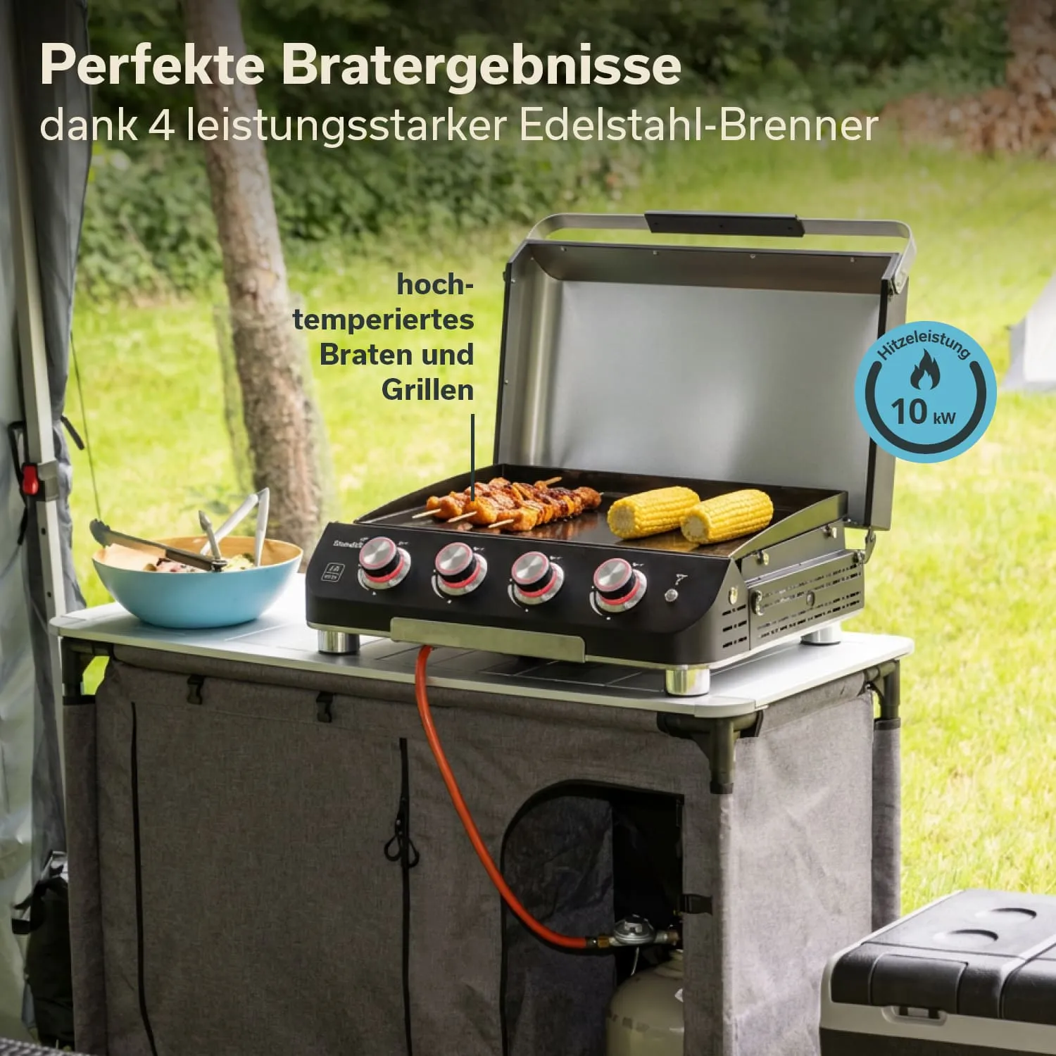 Grill mit Edelstahl-Brenner, Essenszubereitung auf einer Plattenfläche, neben einem blauen Geschirr mit Salat.