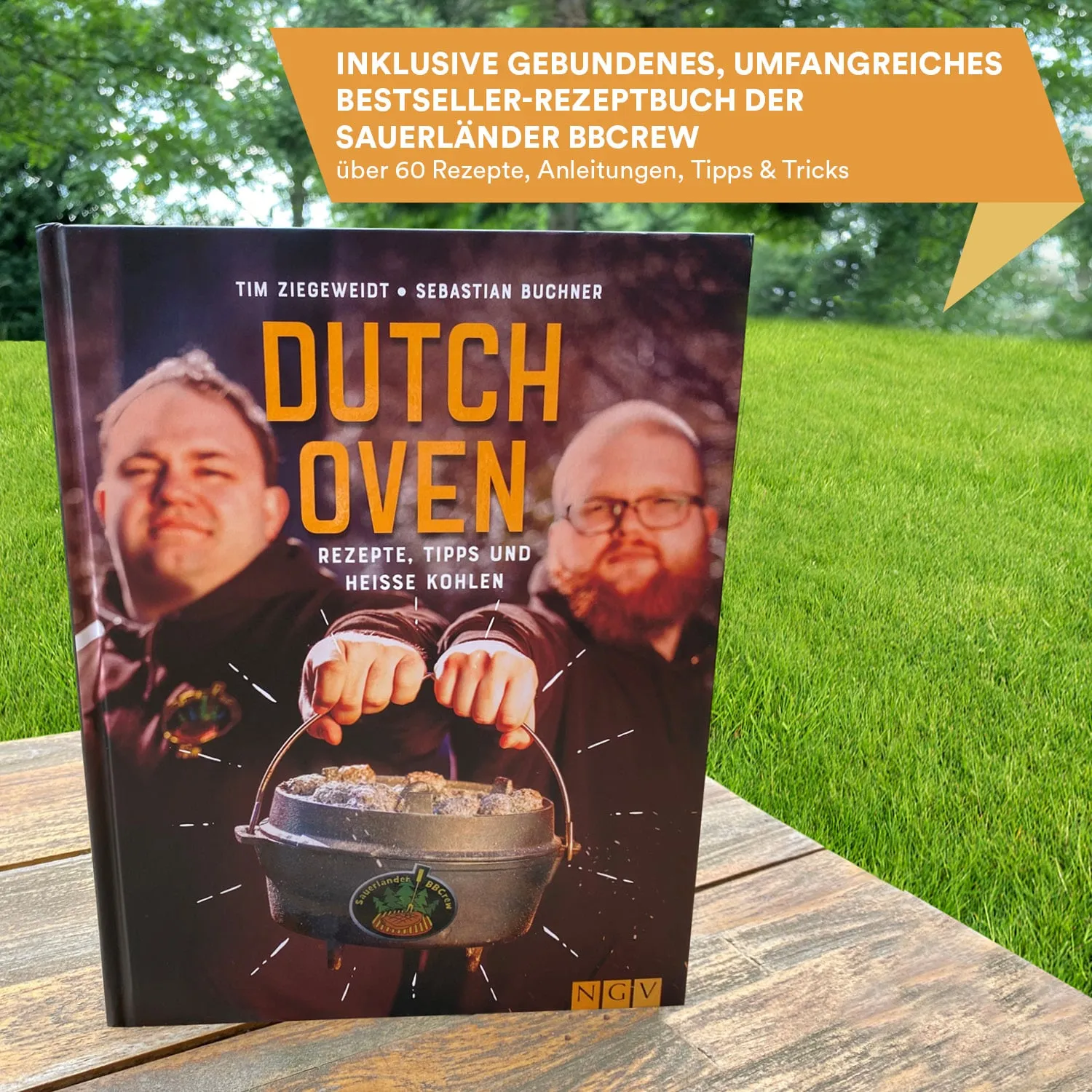 Ein Kochbuch mit dem Titel "Dutch Oven" liegt auf einer Holzoberfläche. Im Hintergrund ist grünes Gras sichtbar.