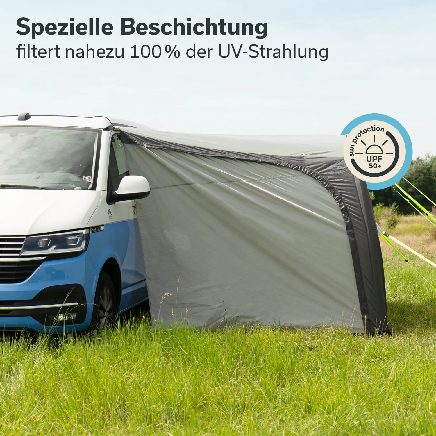 Zeltplane neben einem weißen und blauen Fahrzeug, im Vordergrund grünes Gras, im Hintergrund ein bewaldeter Bereich.