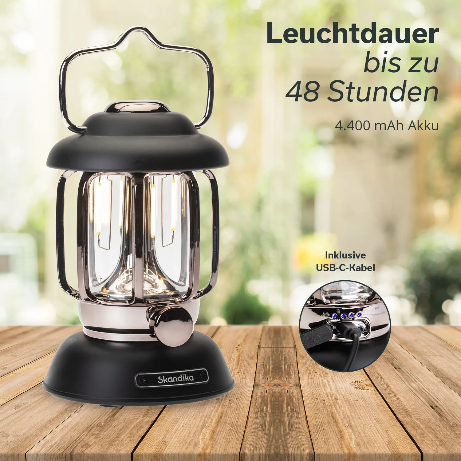 Eine laternenförmige Lampe auf einem Holzstich, mit einem schwarzen Gehäuse und einem silbernen Griff. Im Hintergrund verschwommenes Grün.