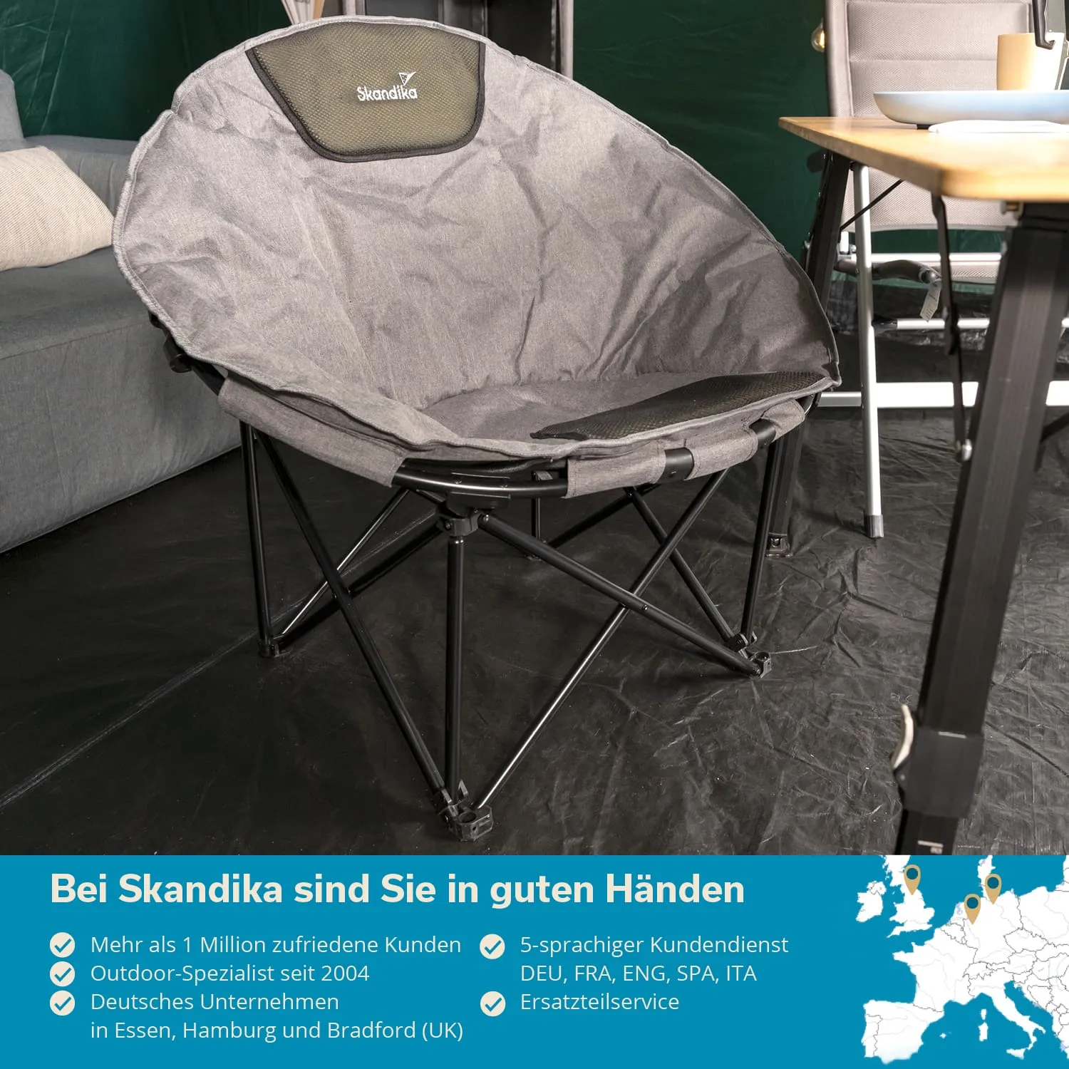 Grauer, runder Faltstuhl mit schwarzem Rückenpolster, neben einem Sofa und einem Tisch in einem Zelt, mit Informationen zur Marke.