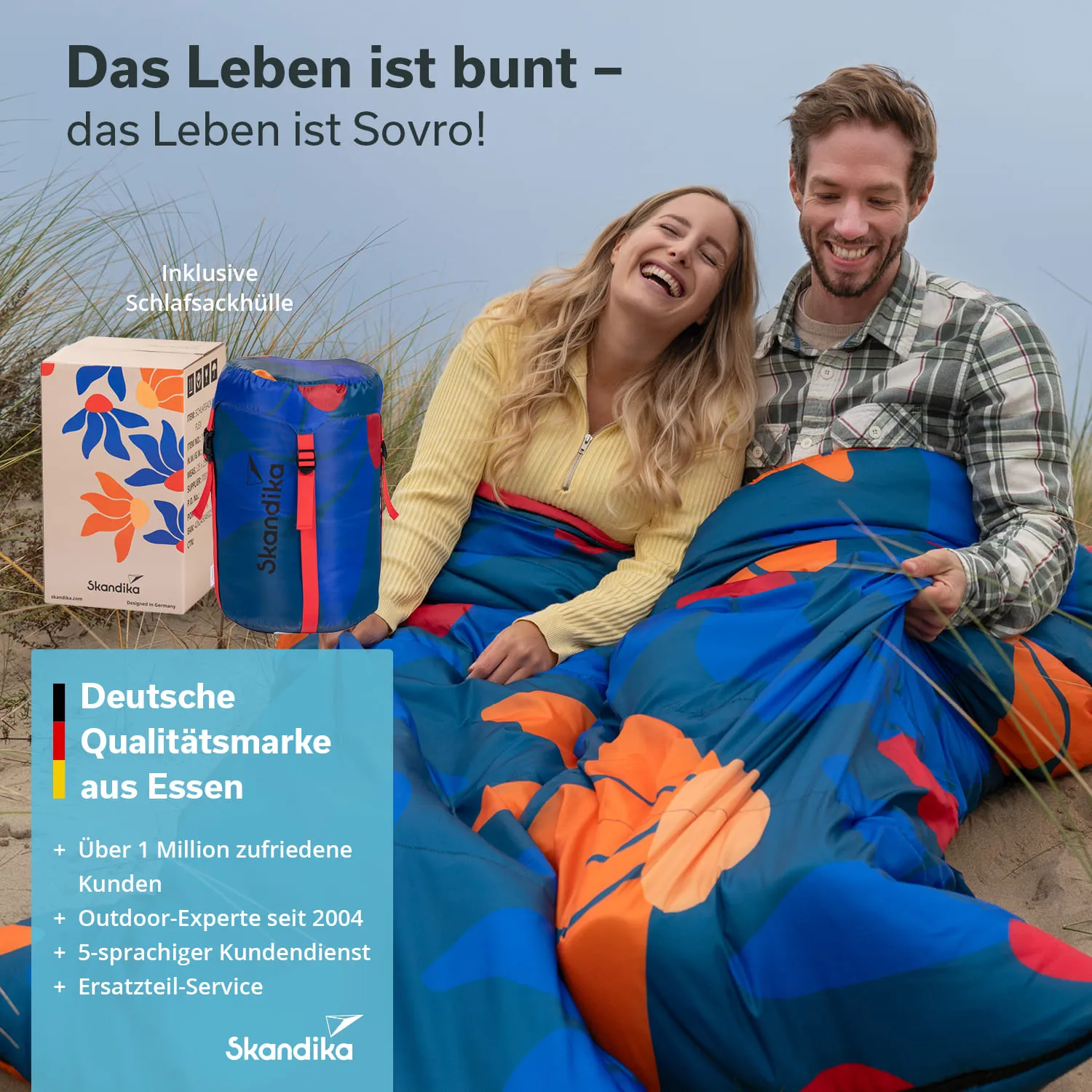 Zwei Personen sitzen im Freien auf dem Boden, eingehüllt in bunten Schlafsäcken. Neben ihnen steht eine Schachtel.