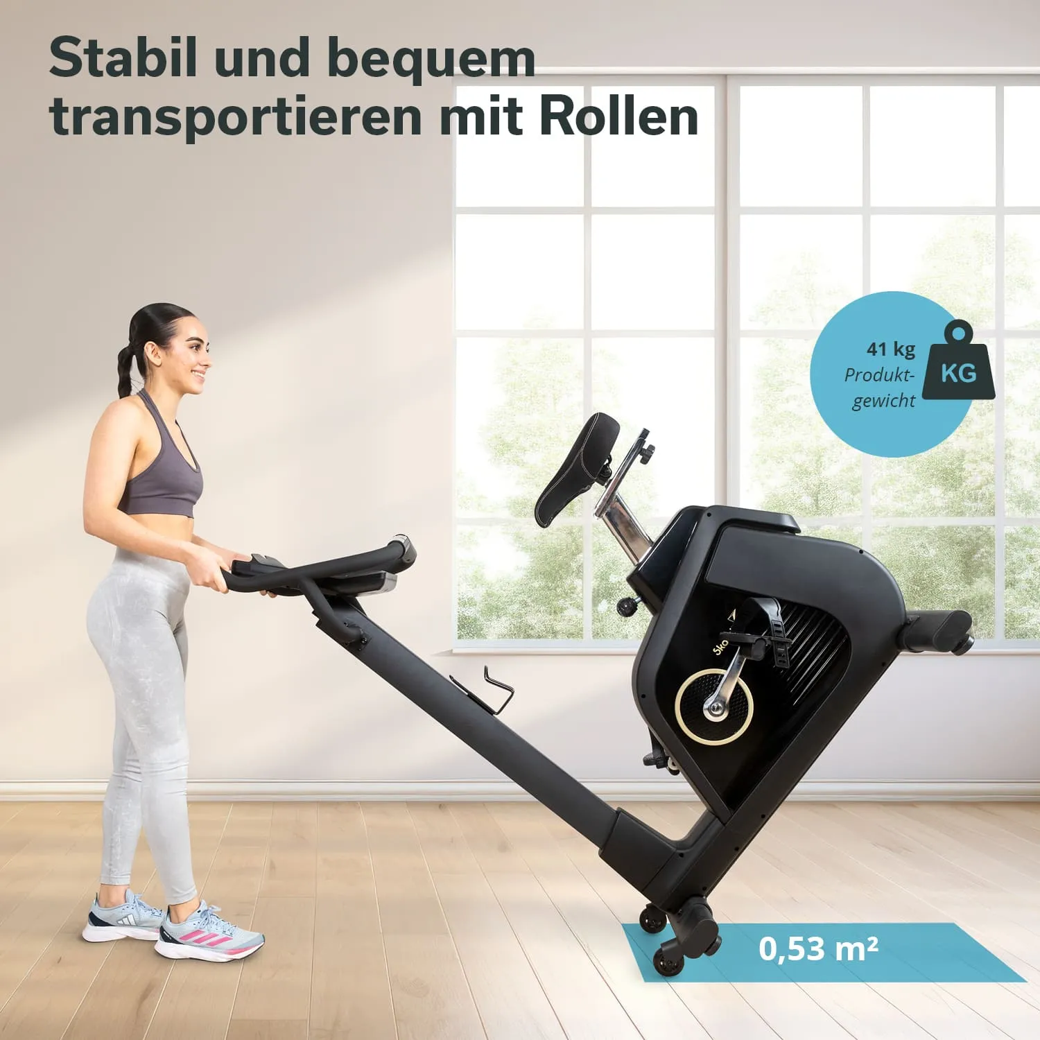 Fitnessgerät mit Rollen, von einer Person bewegt, in hellem Raum mit Fenstern. Produktgewicht und Flächenangabe sichtbar.