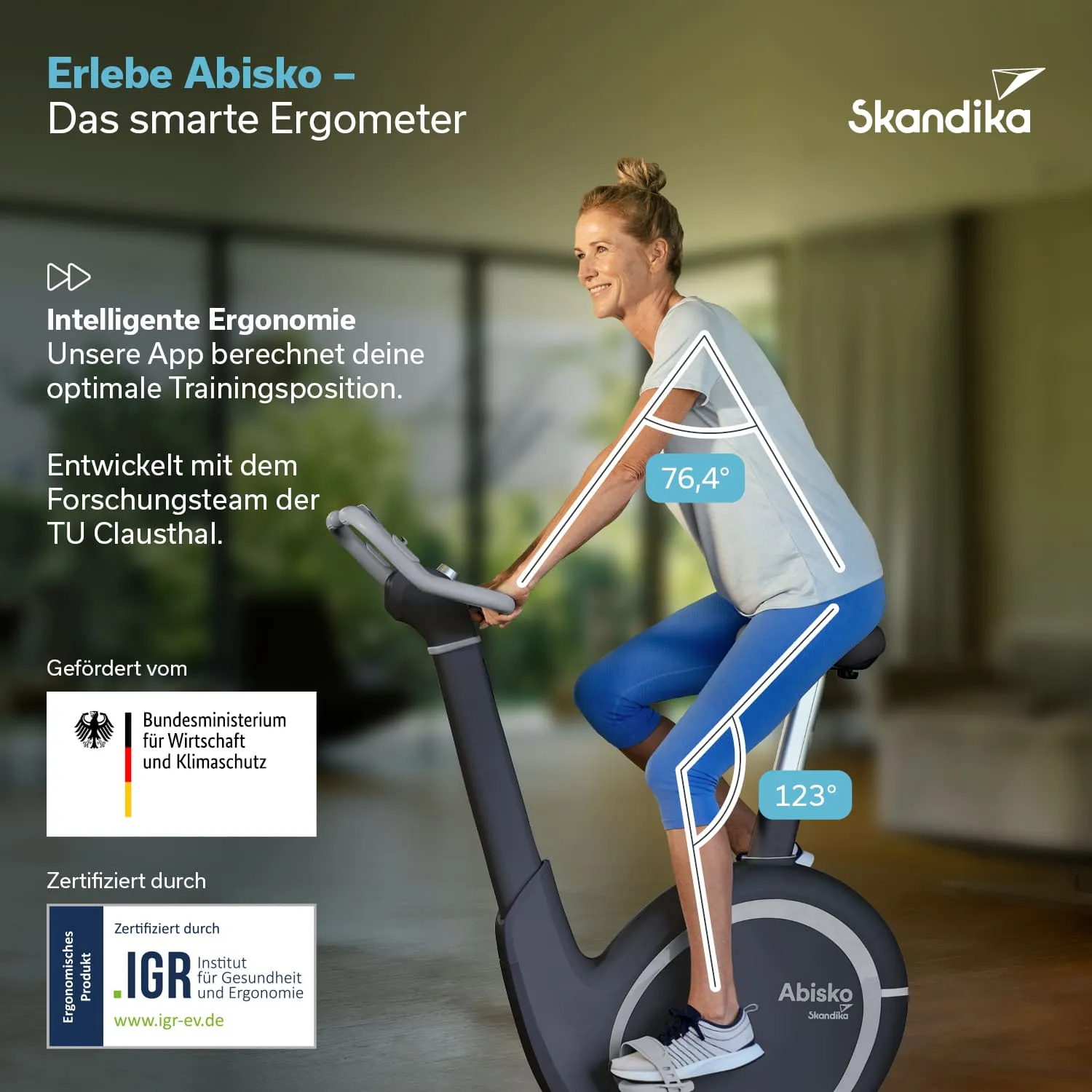 Ergometer mit einer Person, die in Trainingsposition sitzt. Helle Umgebung mit grünen Pflanzen im Hintergrund.