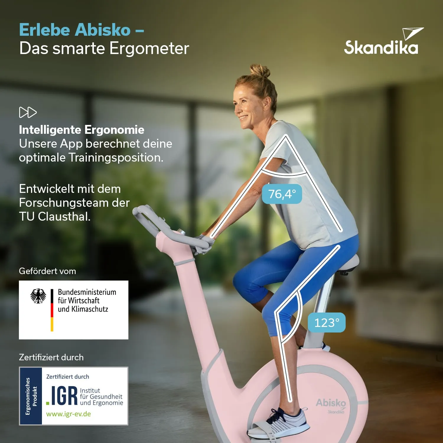 Ergometer in hellem Design mit einer Person, die darauf sitzt. Grüne Pflanzen im Hintergrund.