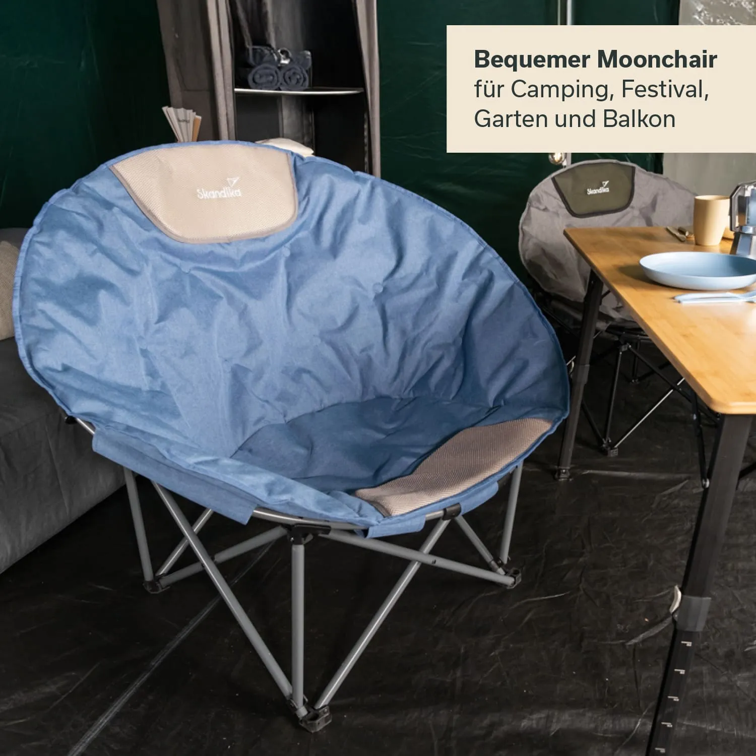 Blauer Moonchair mit einem grauen Bezug steht in einem Zelt. Ein Tisch mit Geschirr ist im Hintergrund sichtbar.