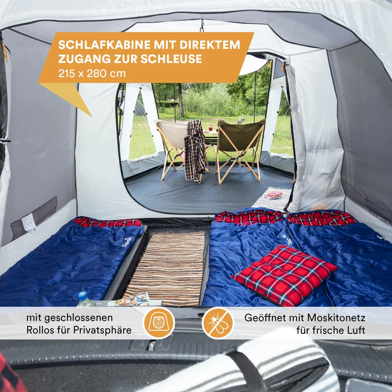 Schlafkabine mit zwei blauen Schlafsäcken und einem Teppich. Zugang zur Außenseite mit Stühlen und Tisch.
