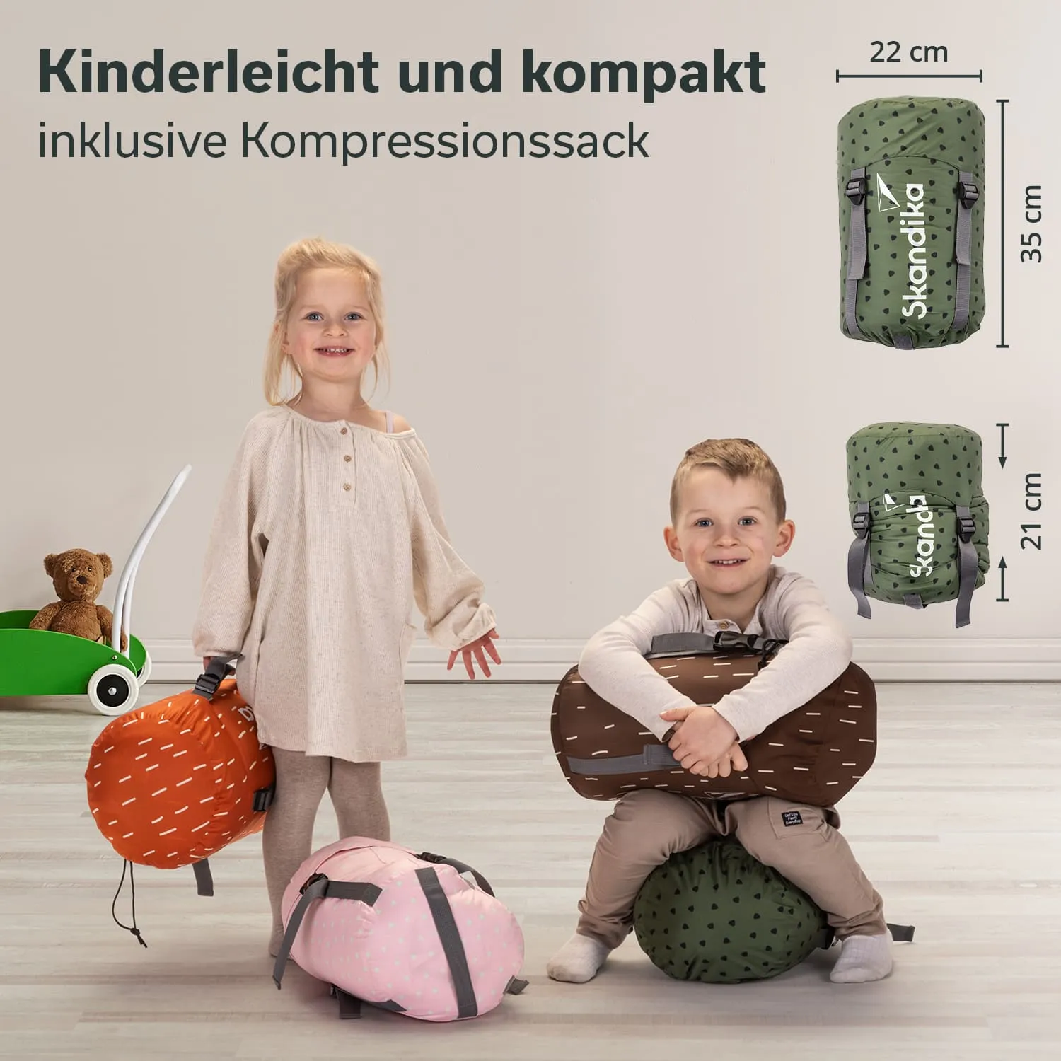 Zwei Kinder stehen in einem hellen Raum neben bunten, gepackten Rucksäcken. Ein Teddybär ist sichtbar.