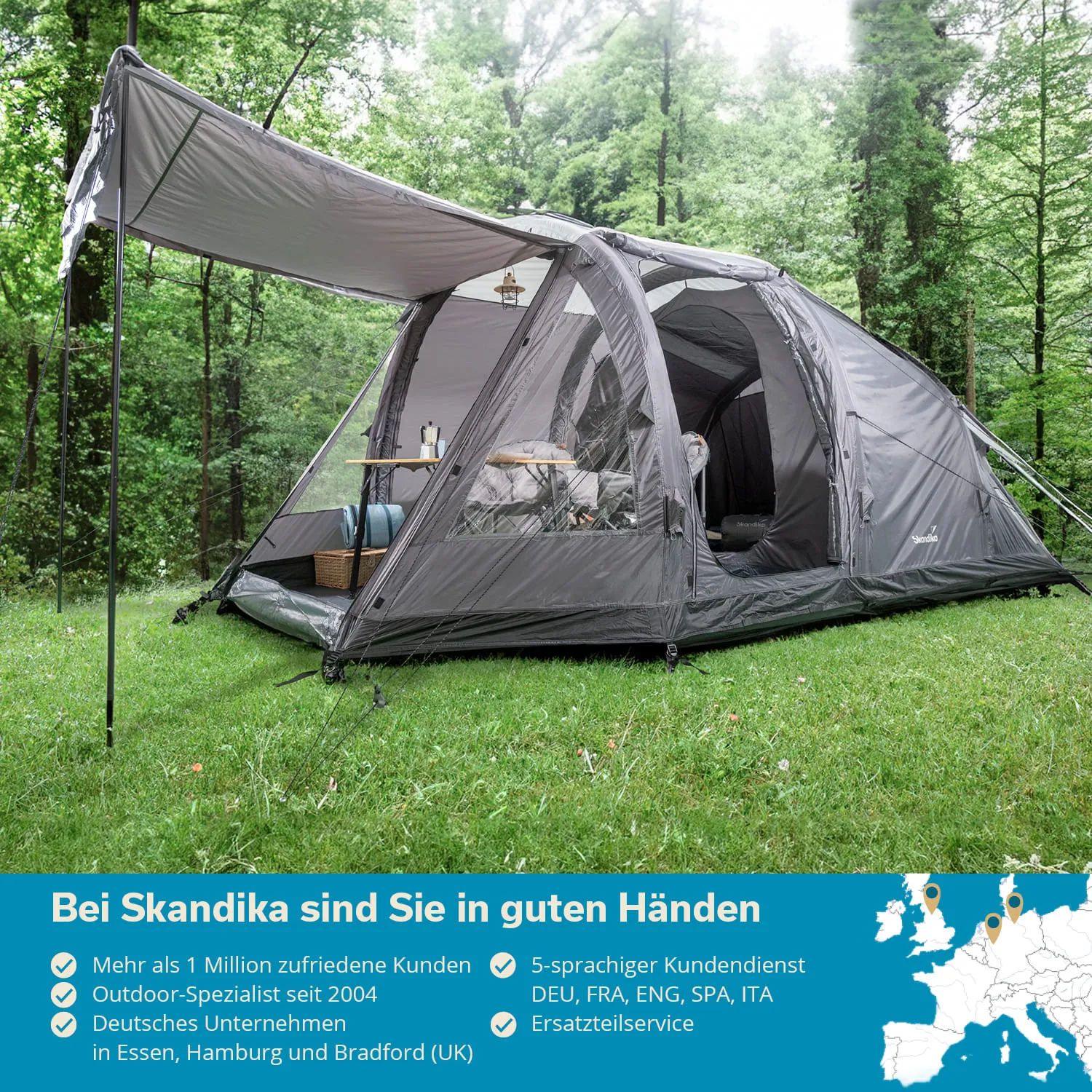 Graues Zelt auf einer Wiese im Wald, mit einem Tisch und Stühlen im Inneren. Bäume im Hintergrund.