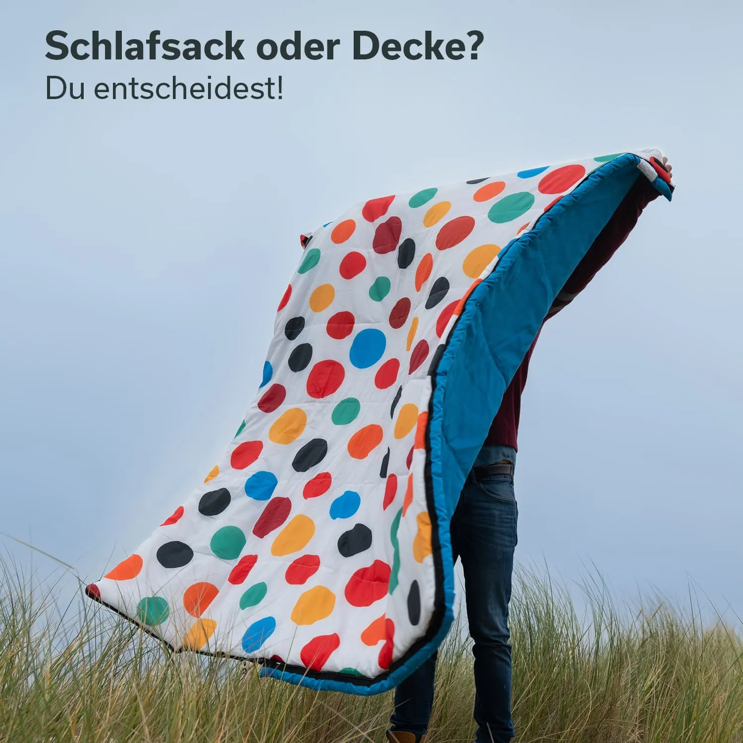 Bunter Schlafsack oder Decke wird von einer Person in der Natur gehalten. Leichter Hintergrund mit bewölktem Himmel.