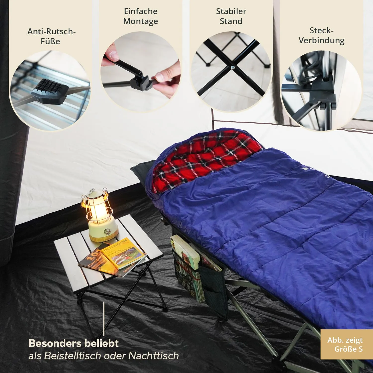 Ein Schlafsack in Blau liegt auf einem Feldbett. Daneben steht ein kleiner Tisch mit einer Lampe und mehreren Büchern.