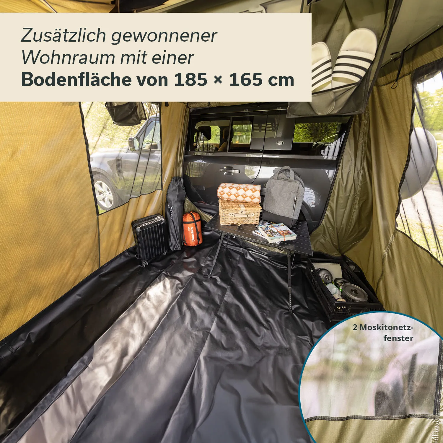Ein Zeltinneres mit einem schwarzen Bodenbelag, ausgestattet mit einem kleinen Tisch und Gepäckstücken. Im Hintergrund ist ein Fahrzeug sichtbar.