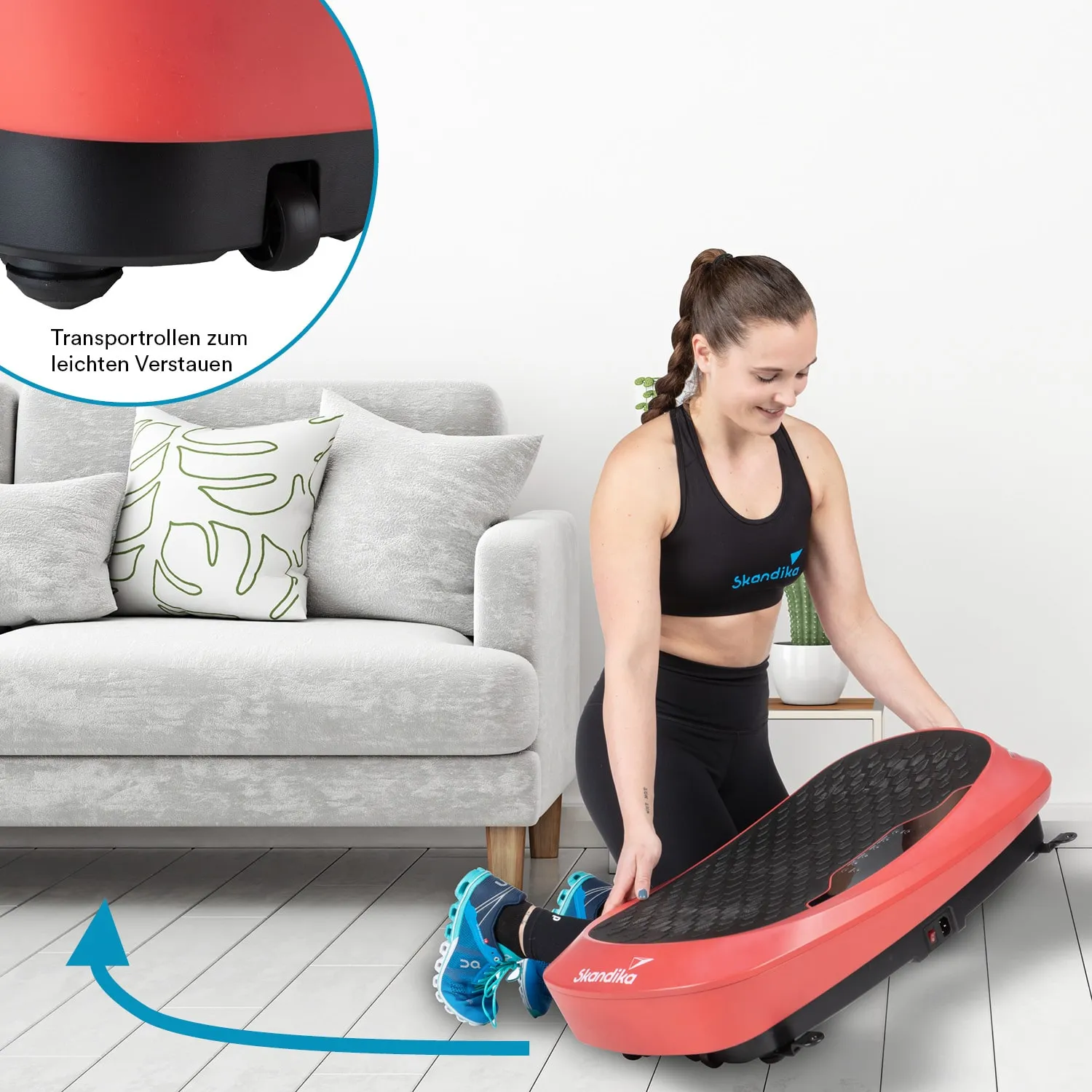 Eine Person kniet auf dem Boden und hebt ein rotes Sportgerät. Im Hintergrund ist ein graues Sofa mit Kissen zu sehen.