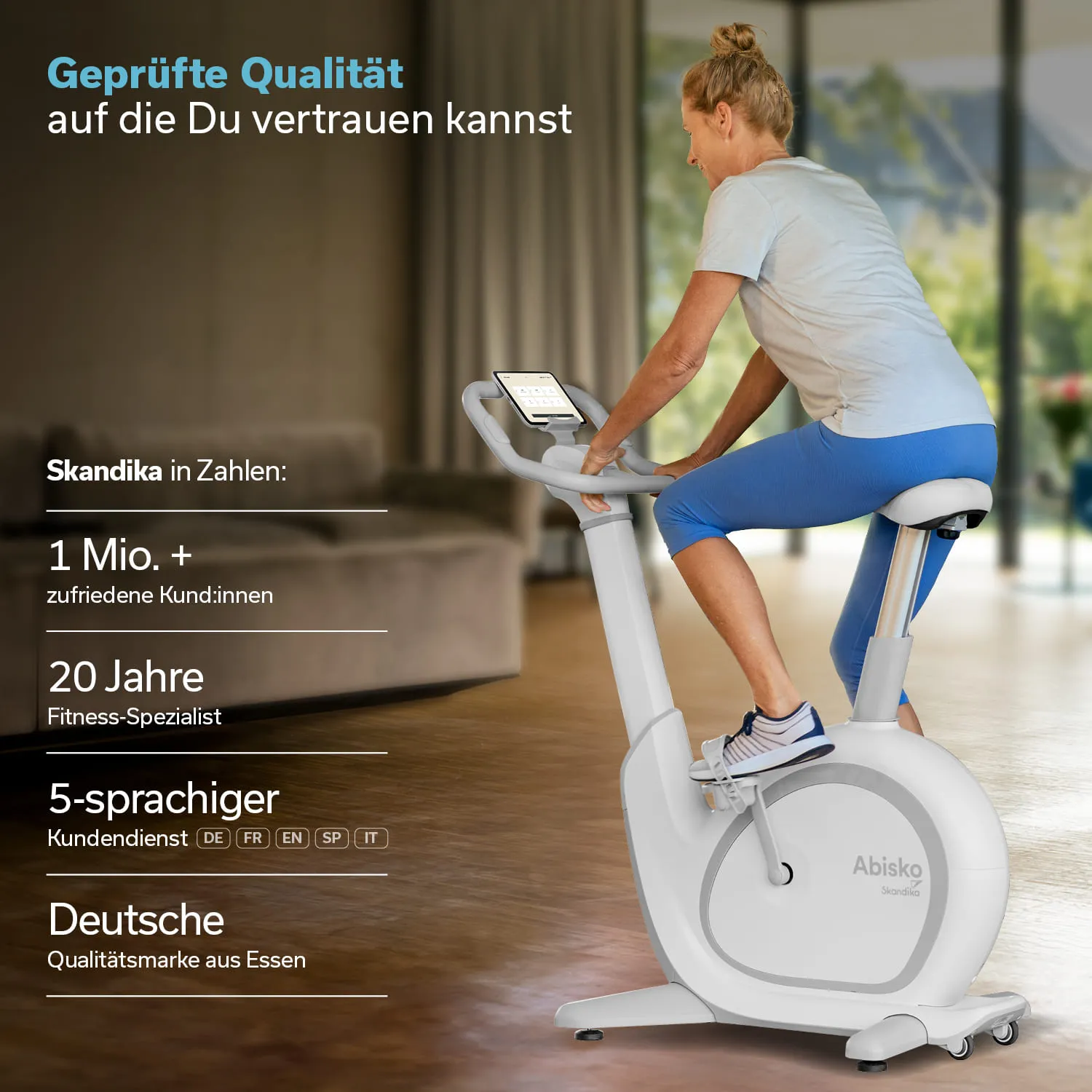 Stationäres Fahrrad mit einem Mann im kurzen Outfit. Display zeigt Trainingsdaten. Heller Raum mit Pflanzen im Hintergrund.