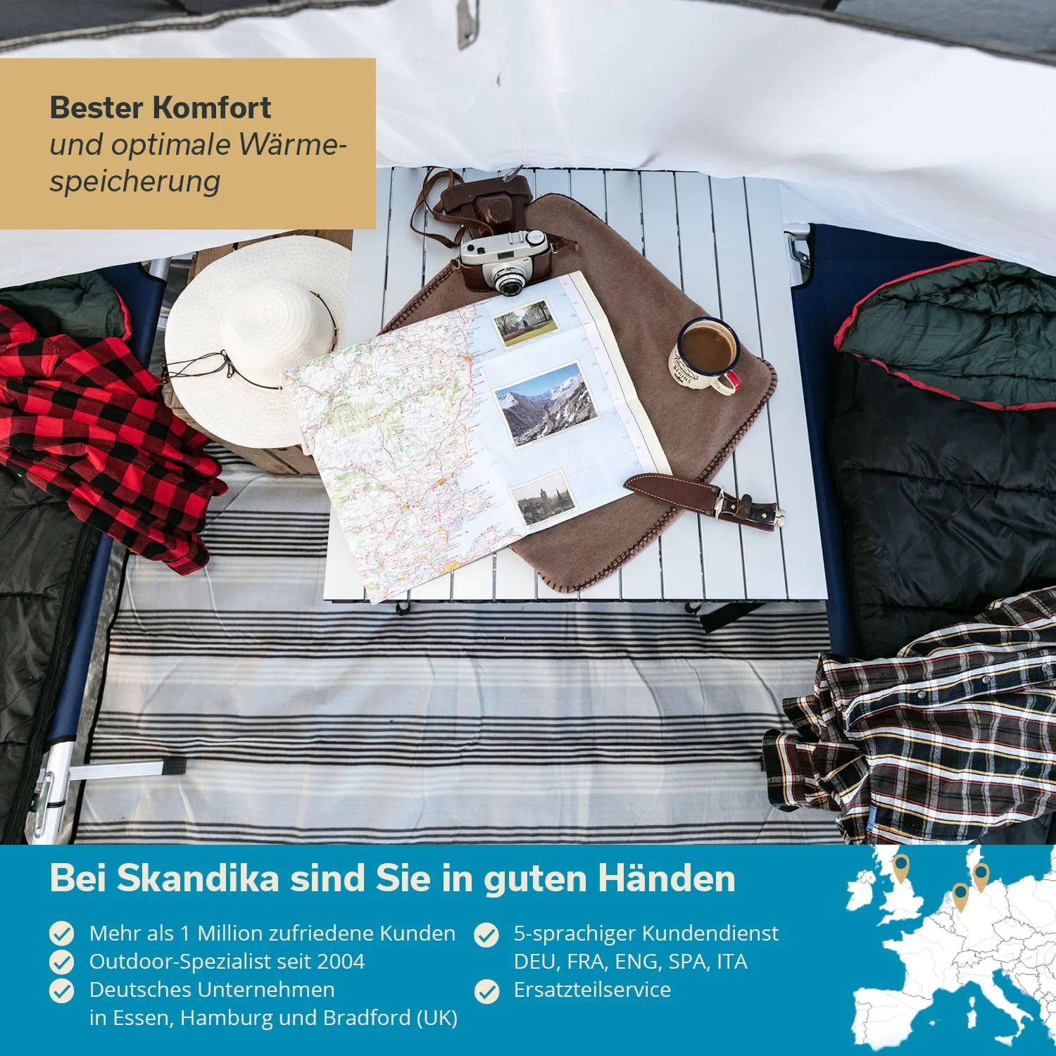 Holztisch mit Karte, Kamera, Tasse und Decke in einem Zelt. Karohemd und Schlafsack liegen daneben.