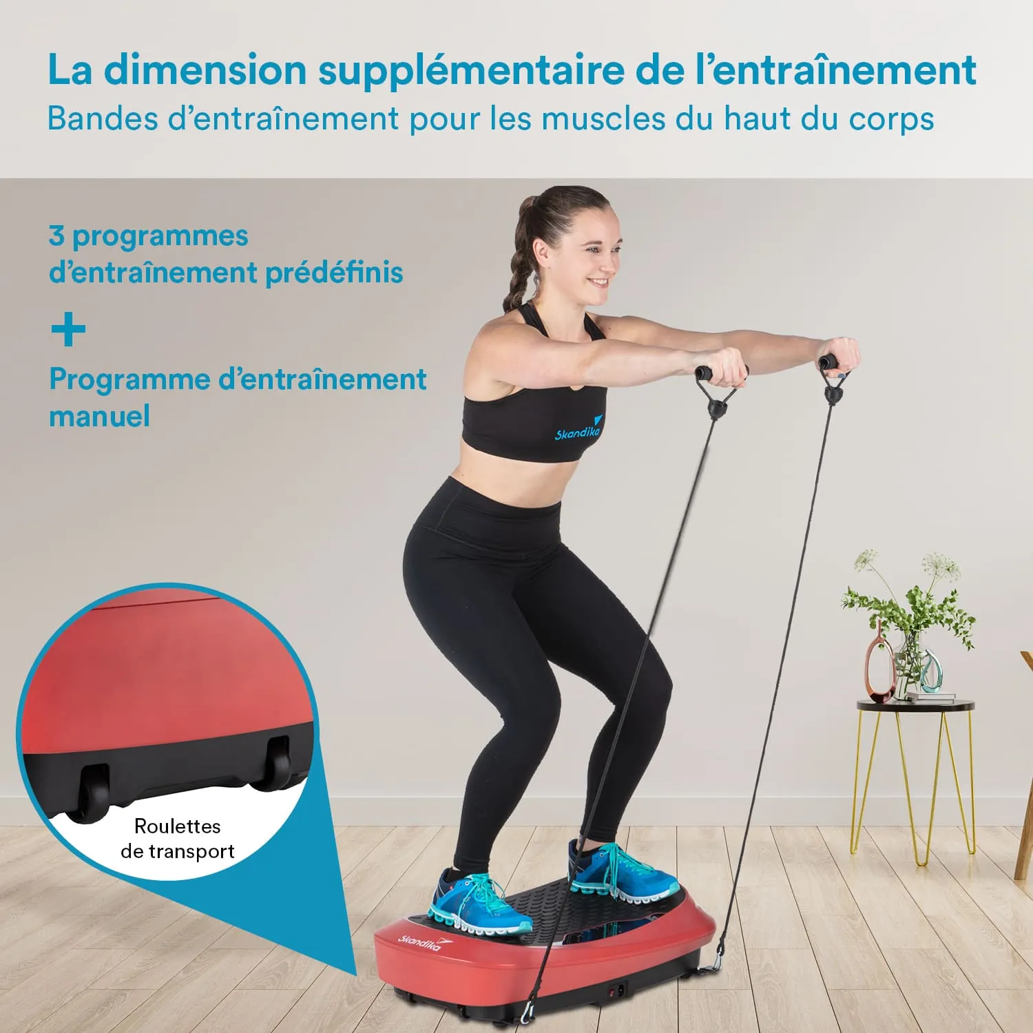 Person steht auf einem roten Trainingsgerät mit Widerstandsbändern, trägt Sportbekleidung und blickt lächelnd nach vorne. Im Hintergrund ein Tisch mit Blumen und Deko.