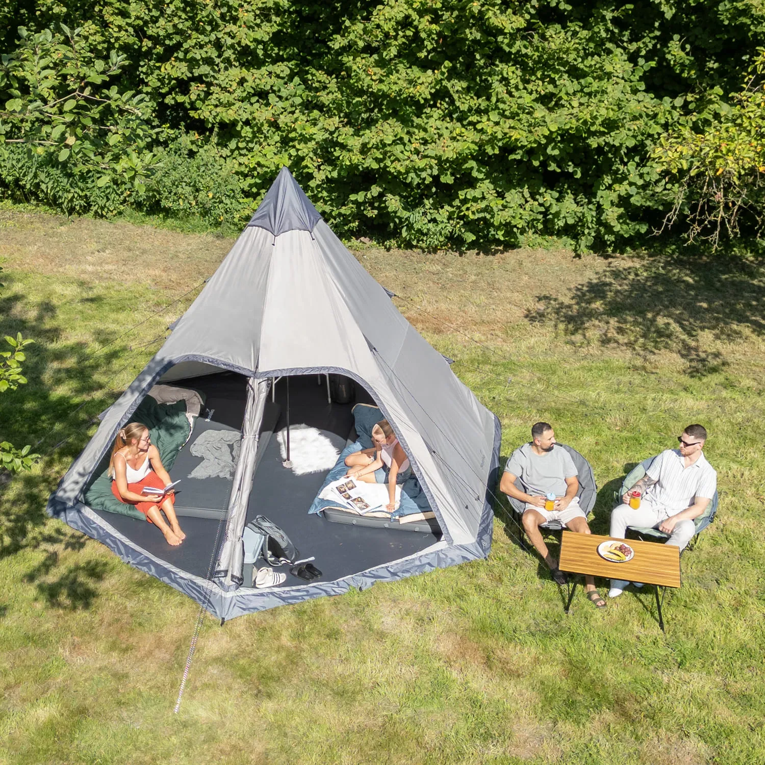 Zelt in einer Wiese mit mehreren Personen, die entspannt sitzen und lesen. Ein Tisch mit Getränken und Snacks ist vorhanden.