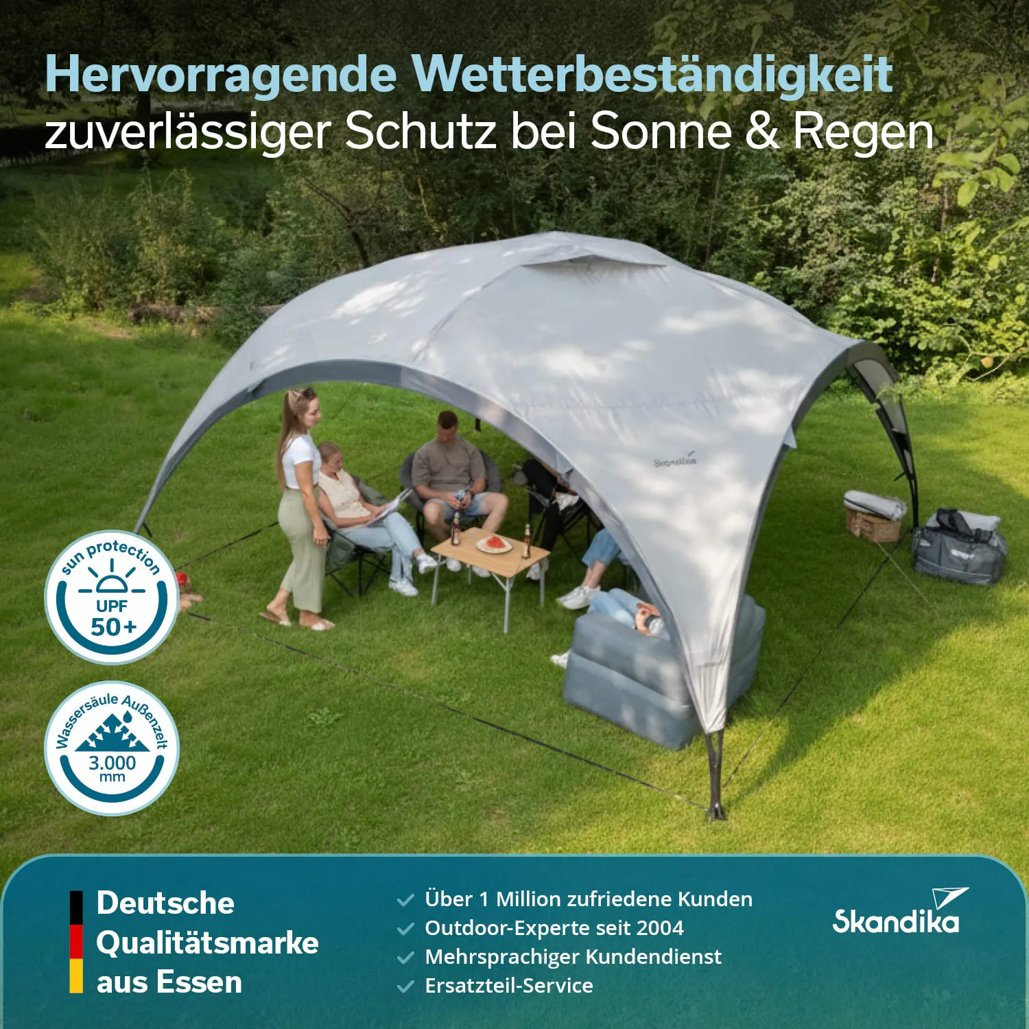 Zelt in einem grünen Garten, darunter sitzen mehrere Personen auf Stühlen. Ein Tisch mit Getränken ist sichtbar.