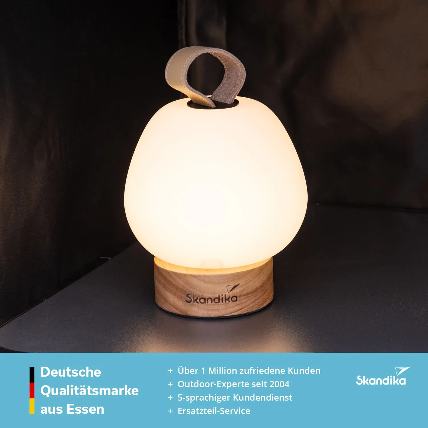 Tischlampe mit milchig-weißer Glaskuppel und Holzfuß. Oben mit einem Lederriemen zum Tragen. Heller, neutraler Hintergrund.
