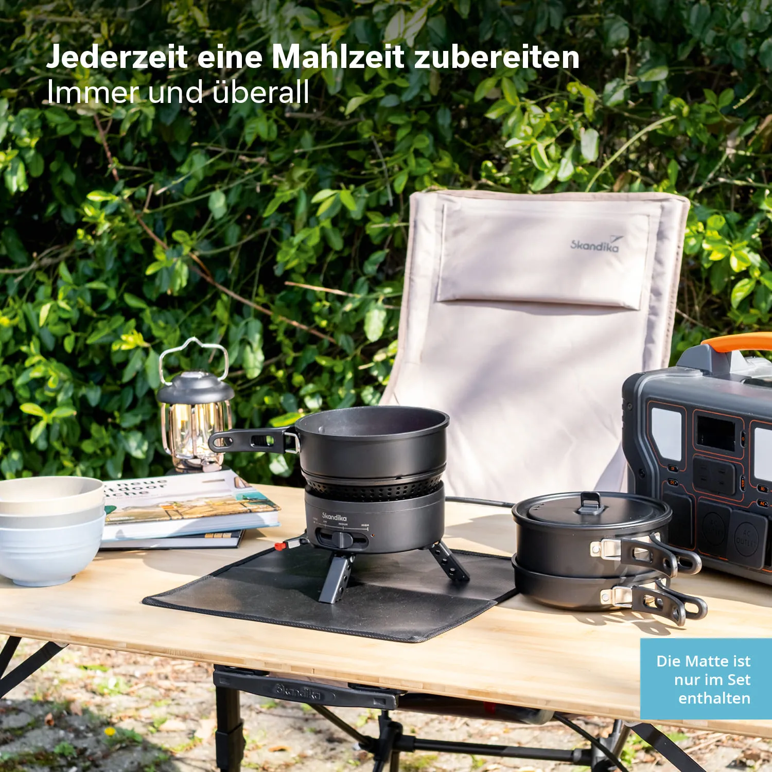 Kochutensilien auf einem Tisch im Freien: ein Kocher, zwei Töpfe, Schalen und eine Laterne, umgeben von grünen Pflanzen.