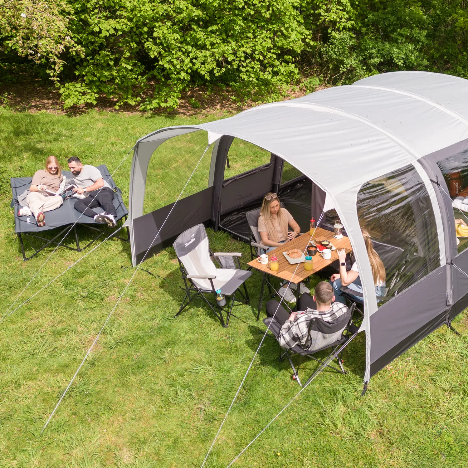 Zelt im Freien mit mehreren Personen in Campingstühlen. Eine Person sitzt an einem Tisch, während andere auf einer Liege entspannen.