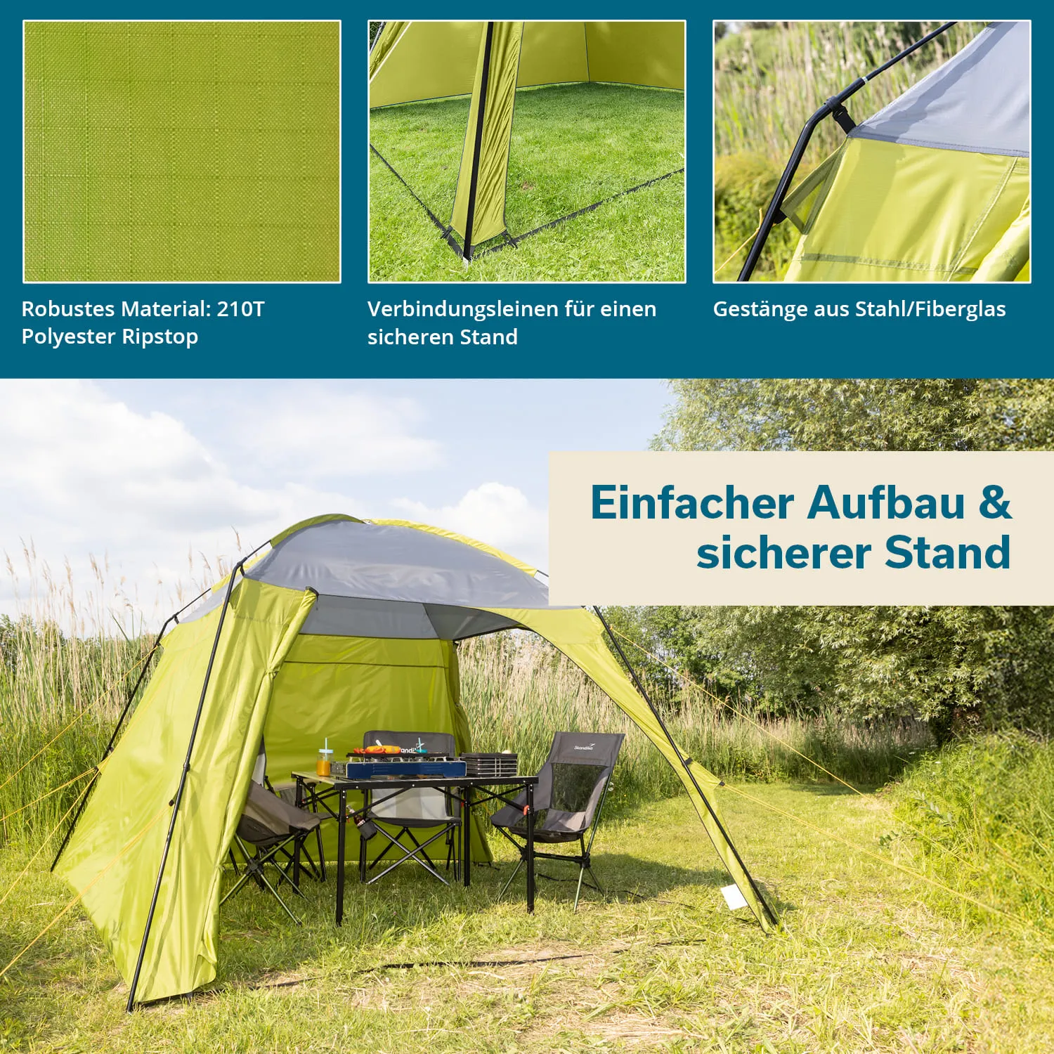 Grünes Zelt mit grauem Dach steht auf Wiese, umgeben von Pflanzen. Tisch und zwei Stühle stehen drinnen.