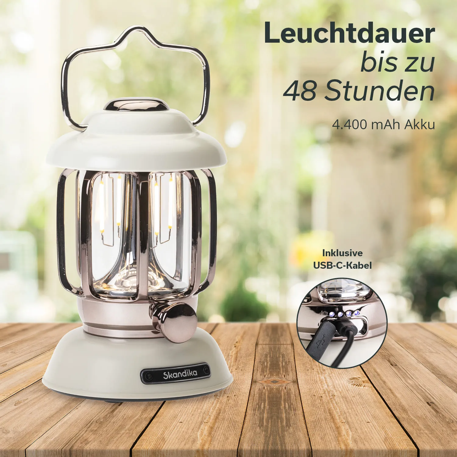 Tischlaterne mit metallischem Gestell, weißen und transparenten Elementen, auf einem Holztisch. Im Hintergrund Pflanzen.