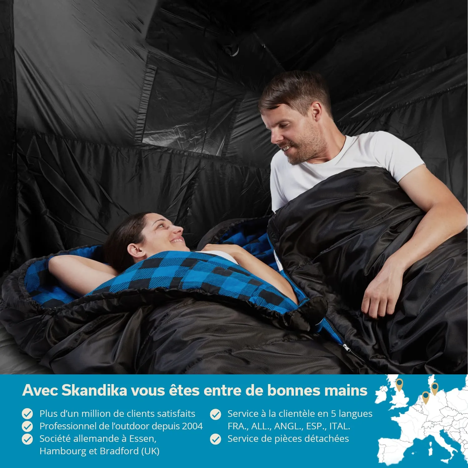 Zwei Personen in Schlafsäcken sitzen in einem Zelt. Die Schlafsäcke sind schwarz mit einer karierten Fütterung. Der Raum ist dunkel.
