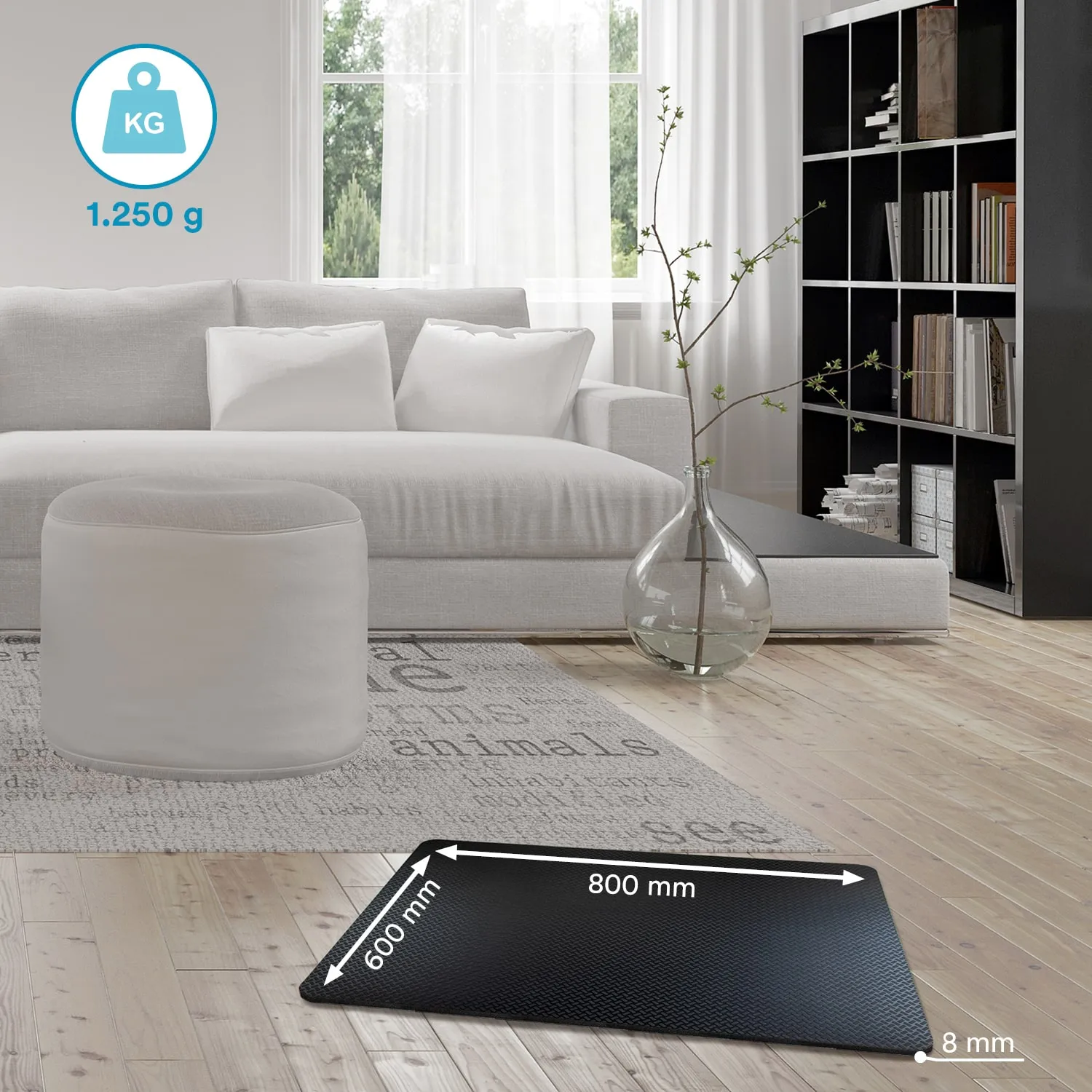 Schwarze Matte mit Maßangaben auf einem Holzfußboden, neben einem grauen Sofa mit weißen Kissen und einem runden Hocker.