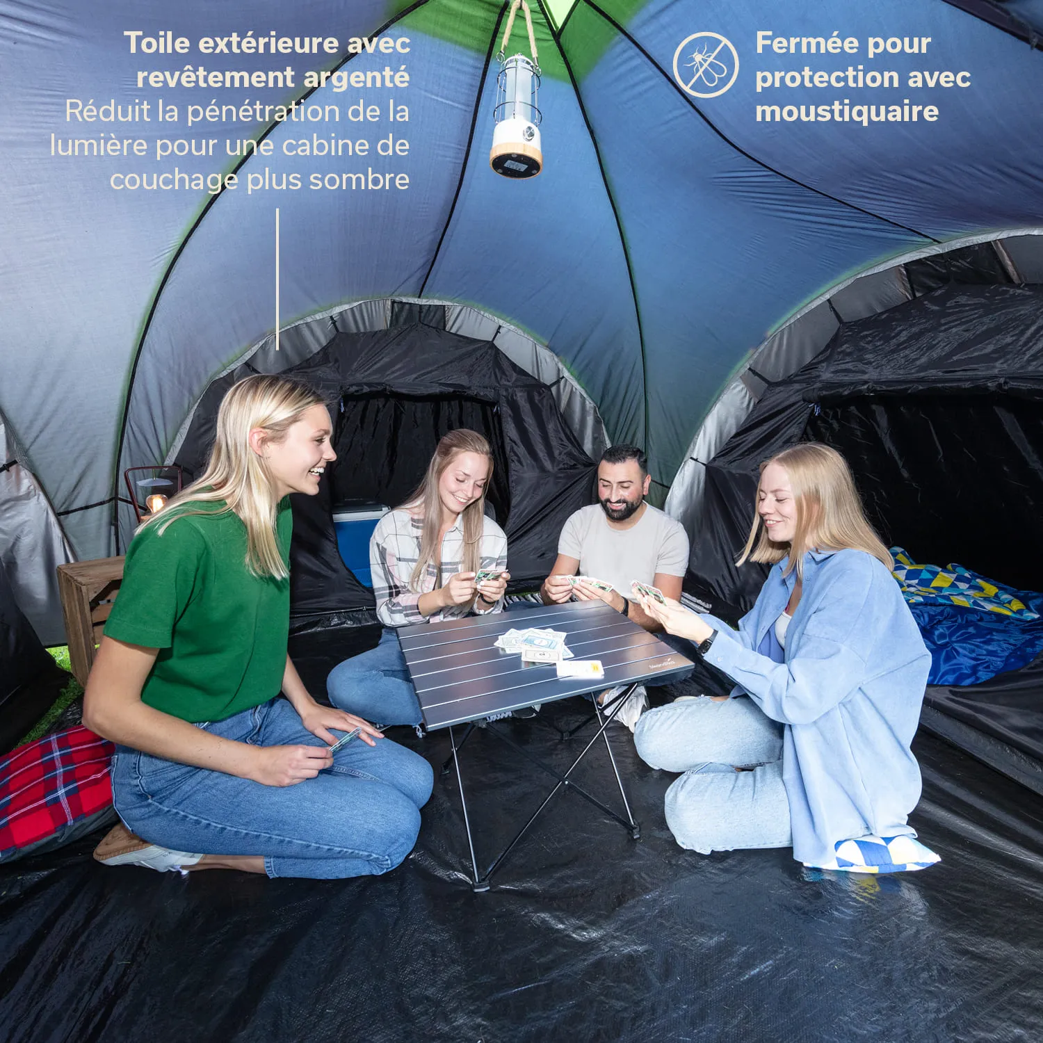 Eine Gruppe von vier Personen sitzt in einem Zelt um einen klappbaren Tisch und spielt Karten. Das Zelt hat eine grüne und graue Innenstruktur.