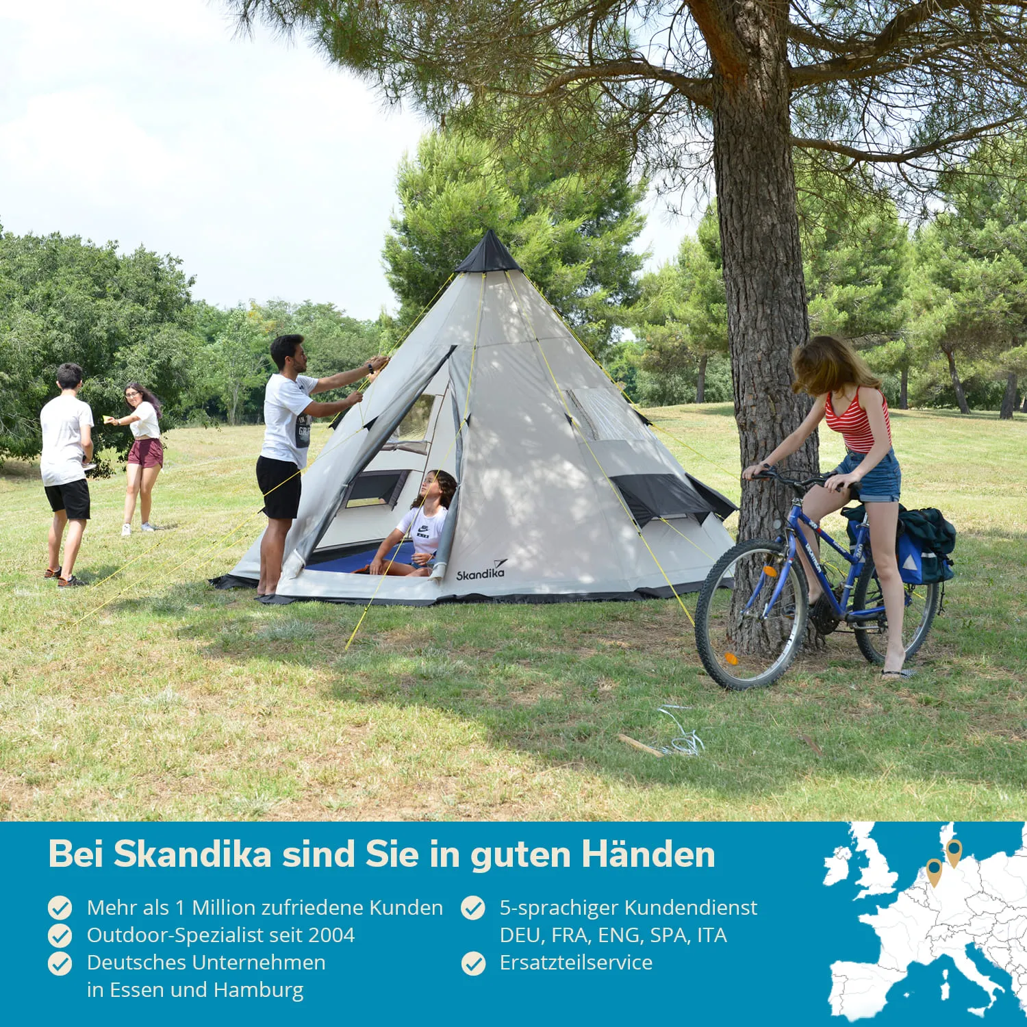 Zelt in einer Wiese, umgeben von Bäumen. Zwei Personen stehen, eine lächelt, während eine andere im Zelt sitzt. Eine weitere Person mit Fahrrad.
