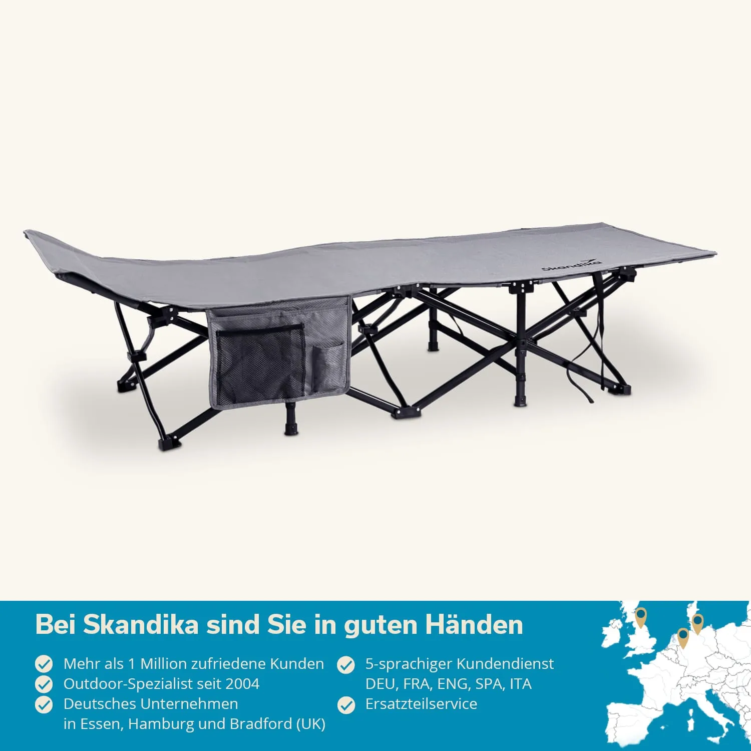 Faltliege in Grau mit schwarzem Gestell und integrierter Tasche seitlich. Hintergrund in hellem, neutralem Farbton.